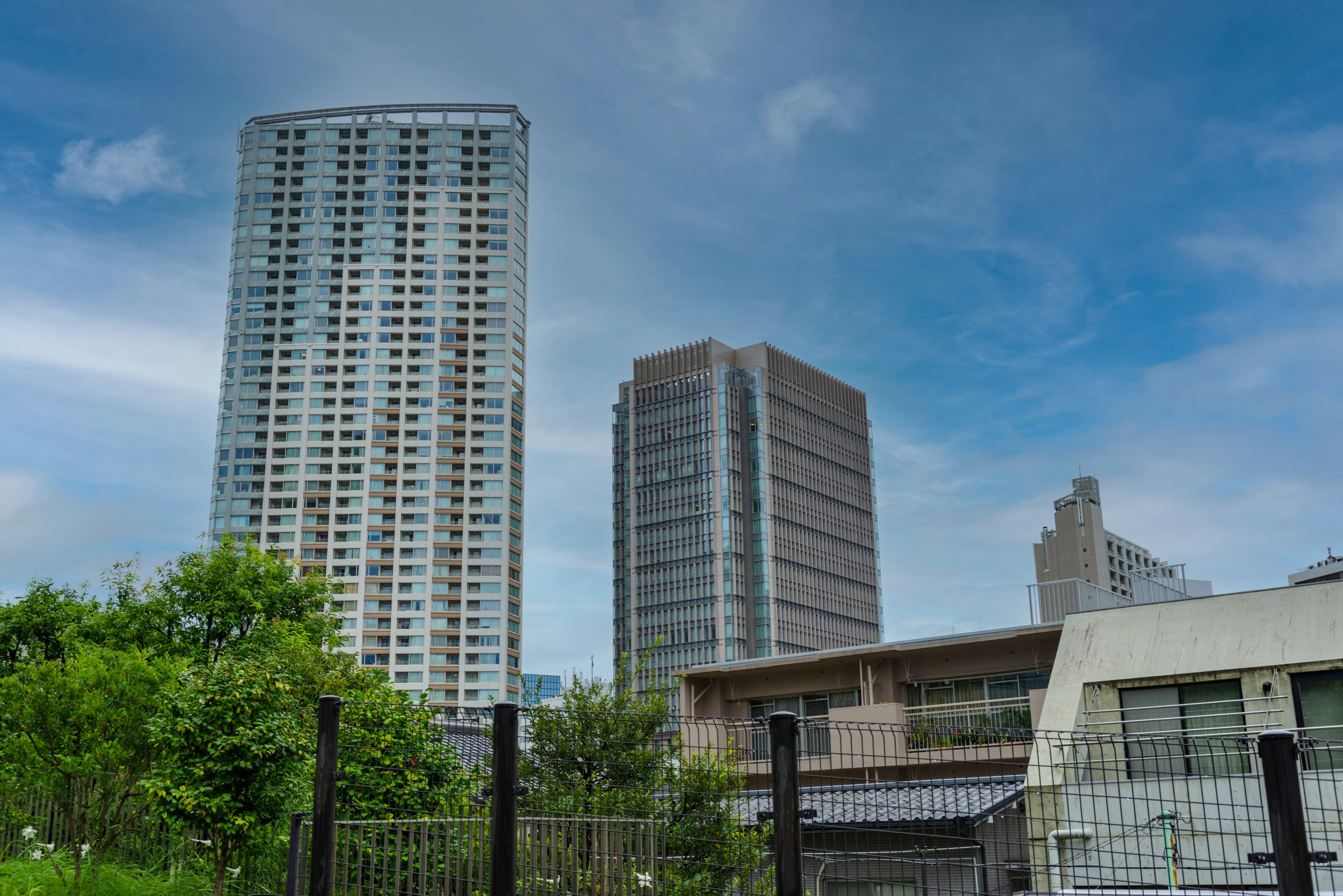 View of tall buildings against a blue sky with greenery in the foreground