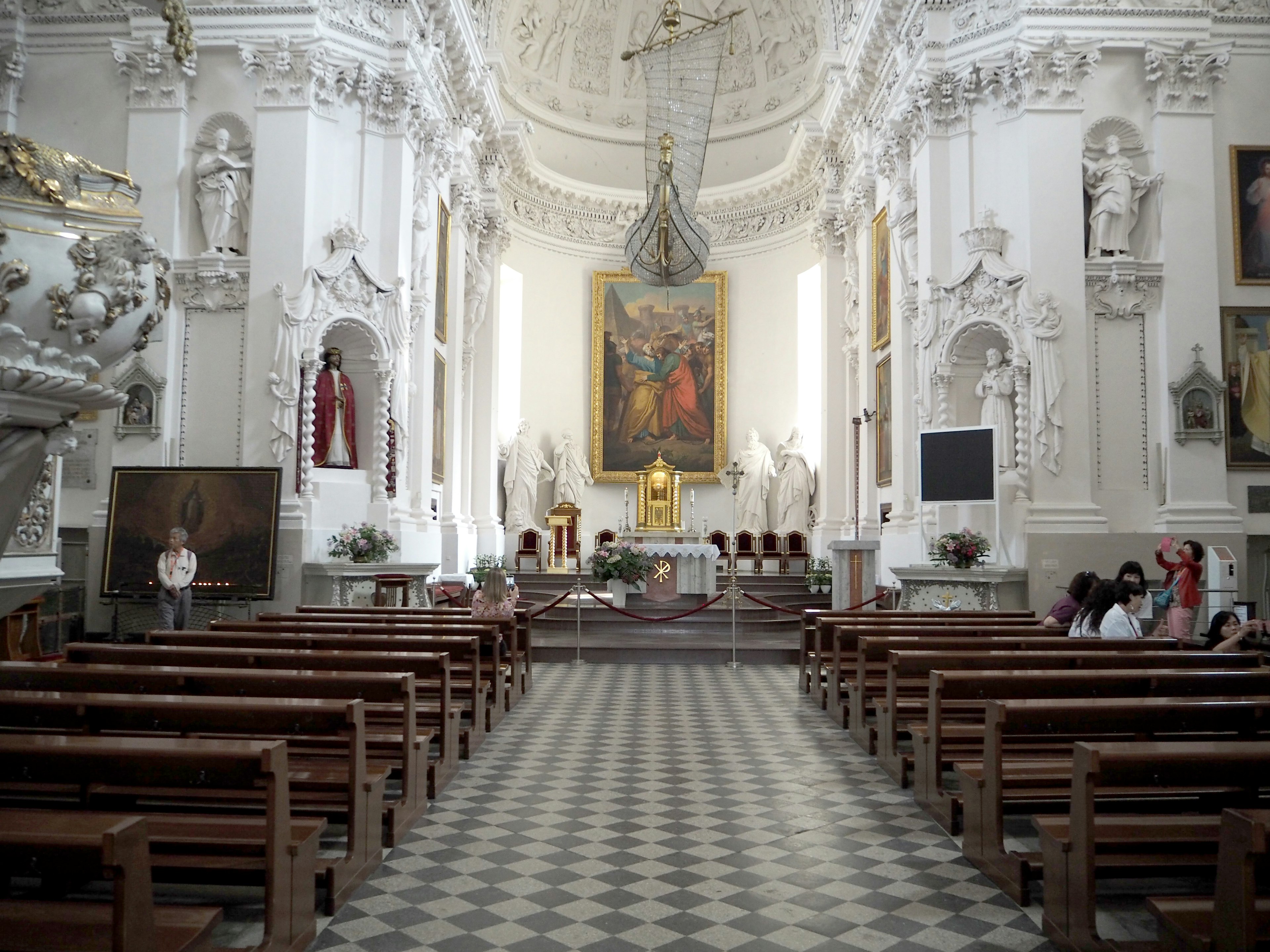 Innenraum einer Kirche mit weißen Wänden mit Reihen von Holzbänken Altar und Gemälde in der Mitte