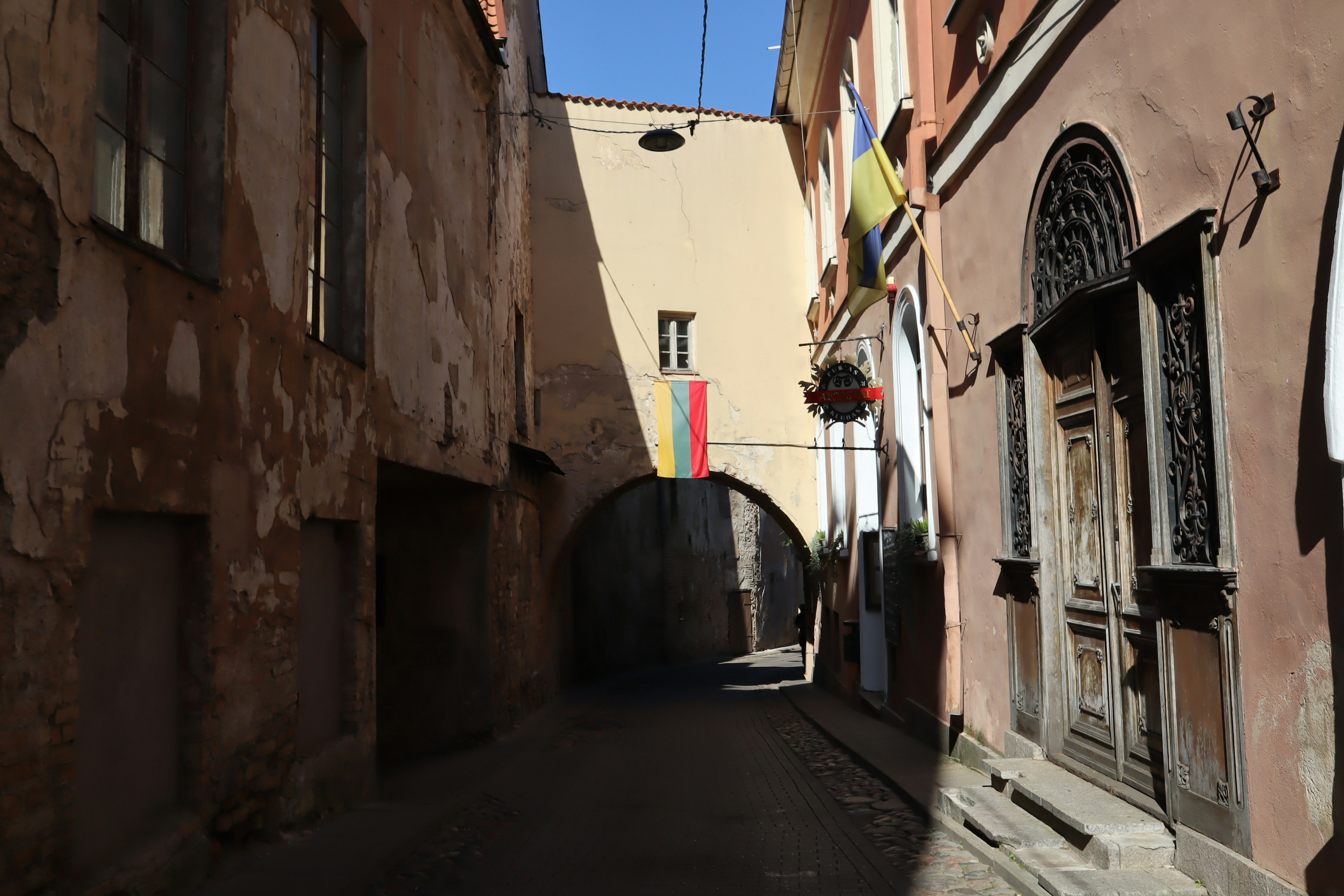 Vicolo stretto con edifici antichi e un arco con una bandiera colorata