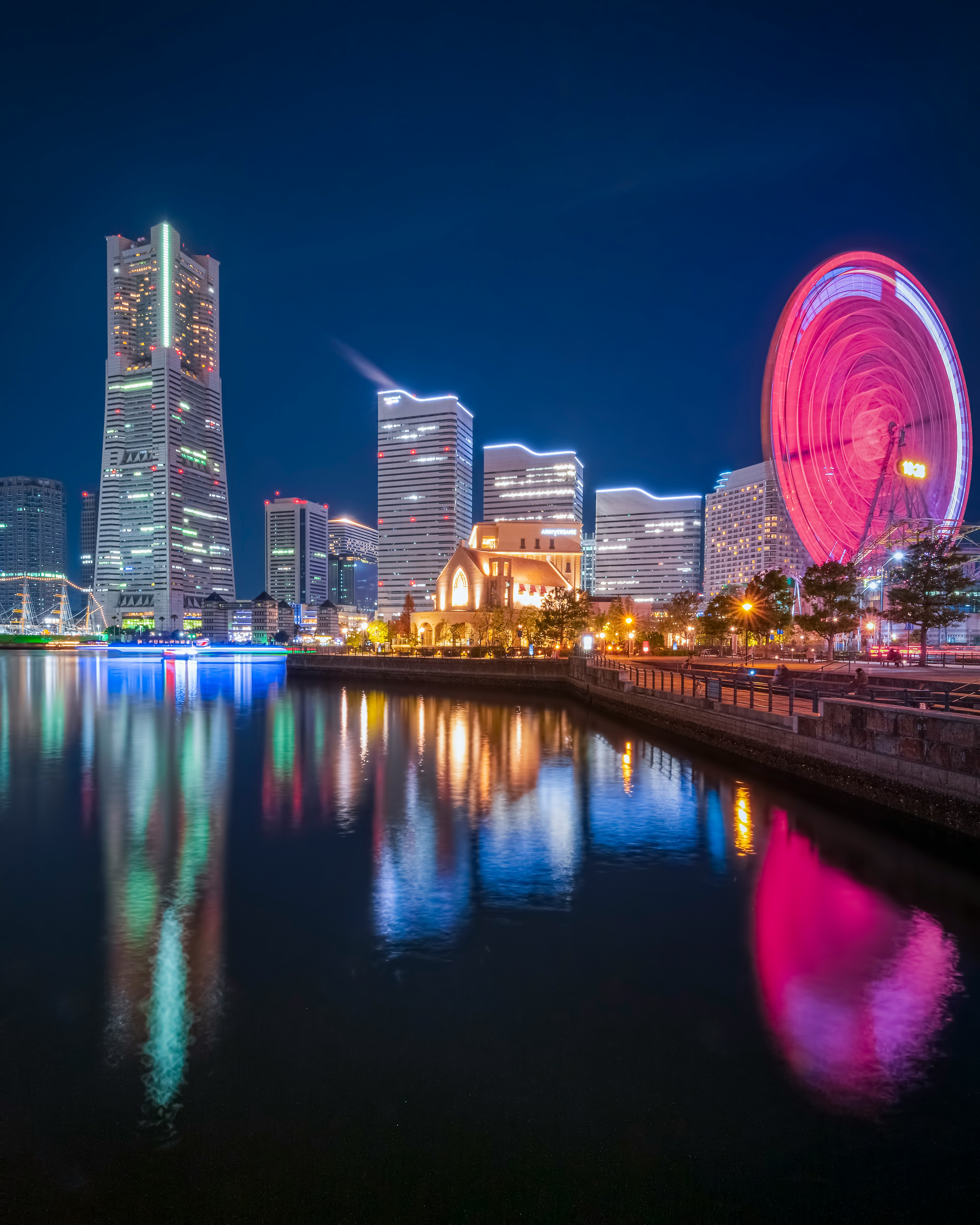 Nachtansicht der Skyline von Yokohama mit beleuchteten Gebäuden und einem Riesenrad, das sich im Wasser spiegelt