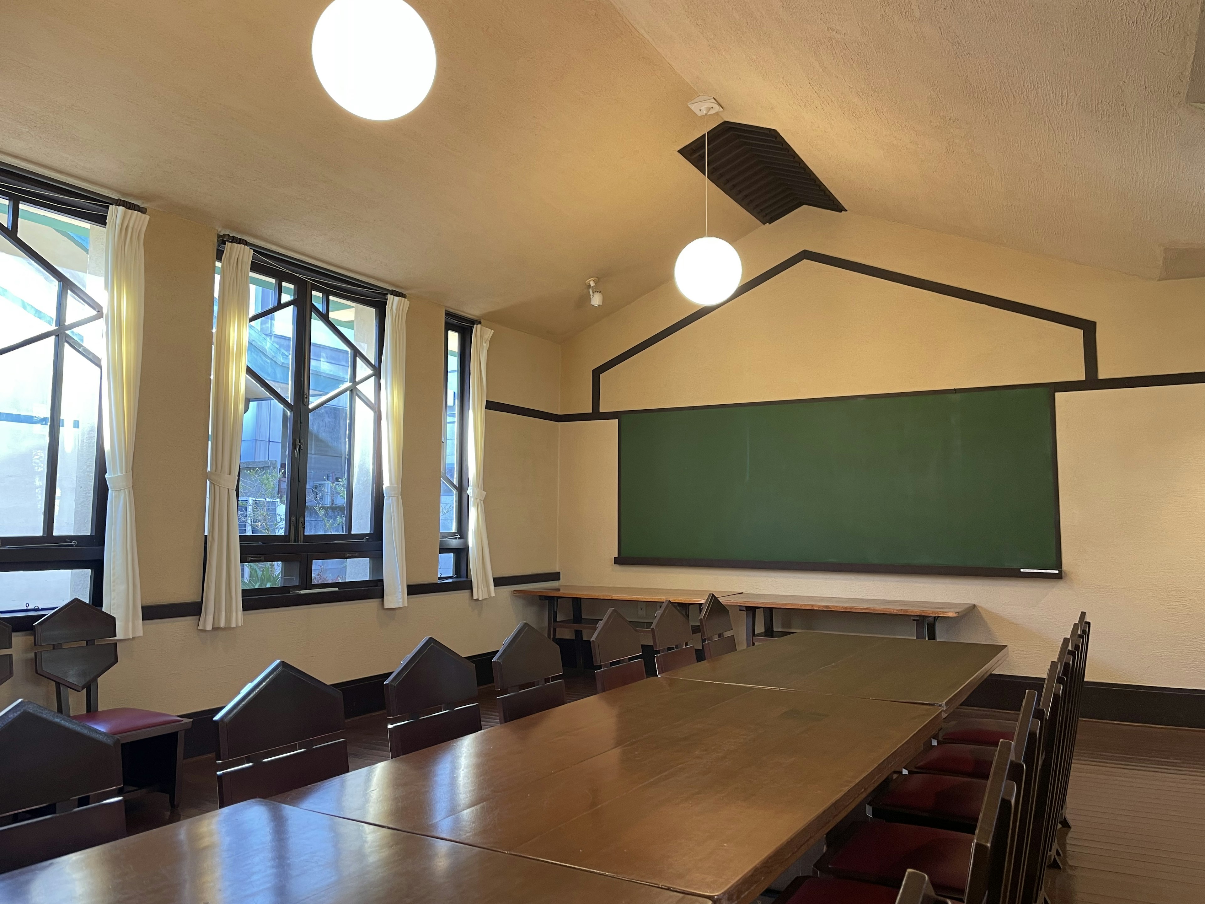 Interior of a classroom featuring a large table with chairs natural light streaming through windows green chalkboard on the wall