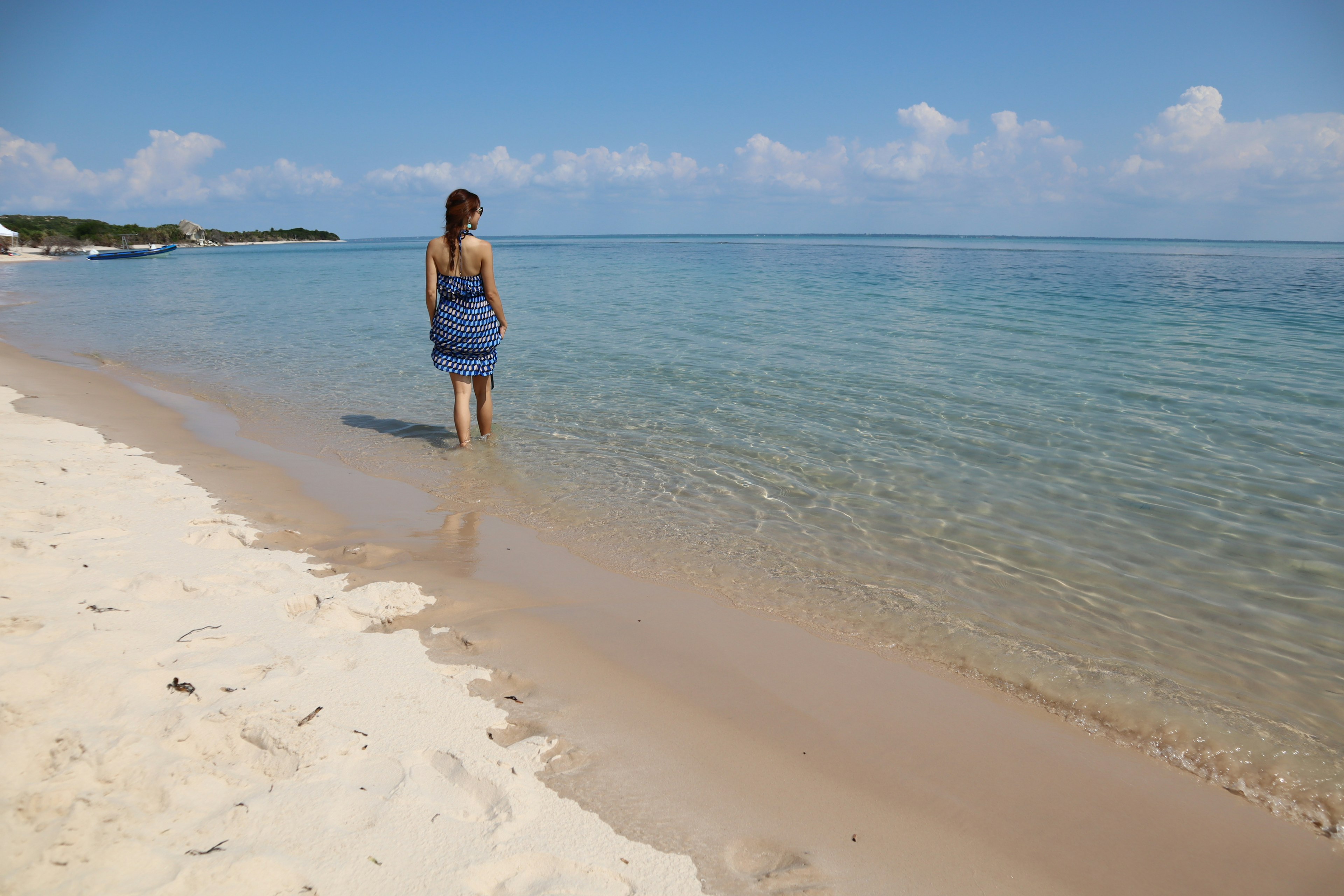 Femme marchant dans l'eau claire sur une plage de sable sous un ciel ensoleillé