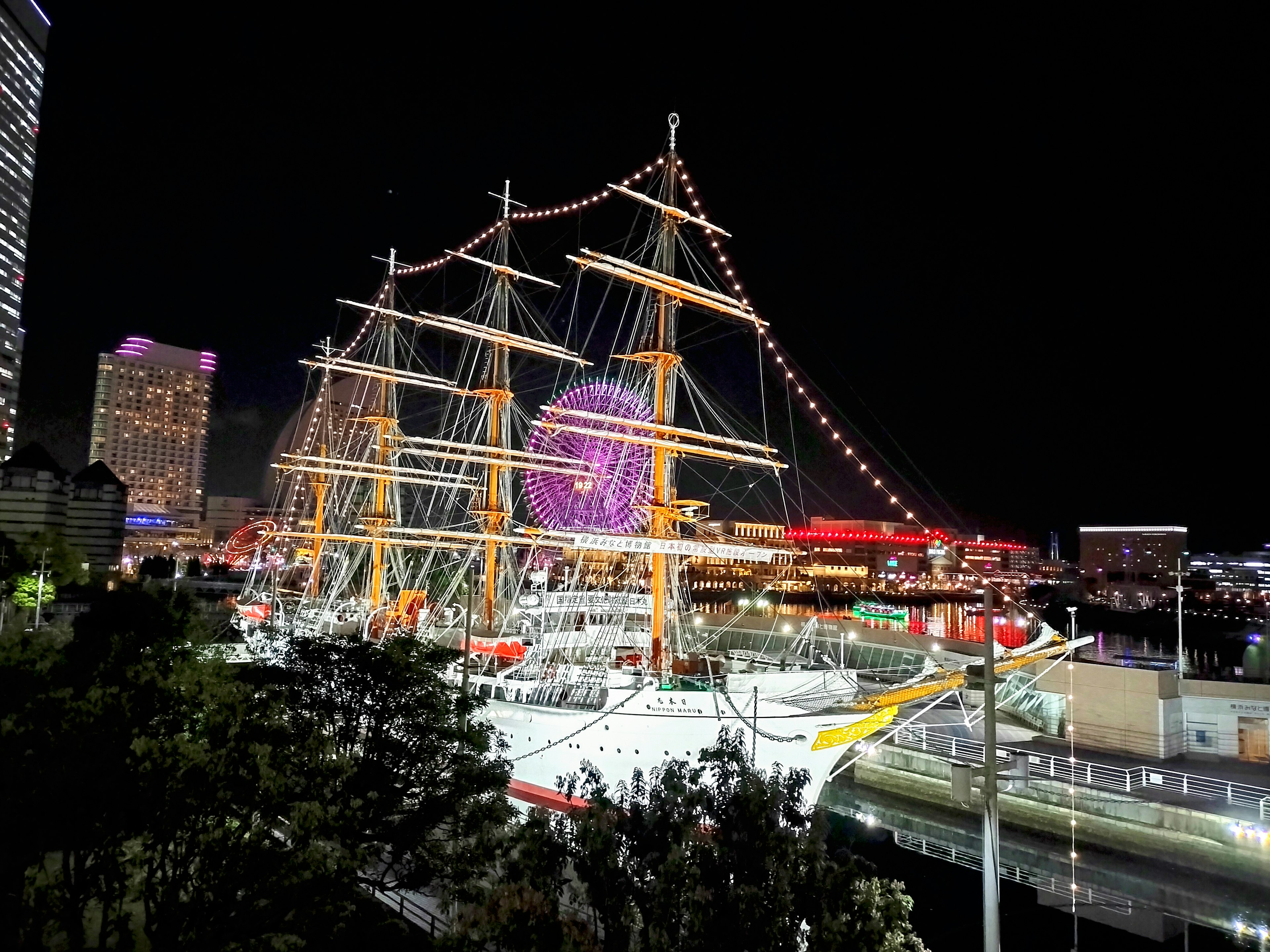 Hermoso barco de vela iluminado por la noche con luces de la ciudad