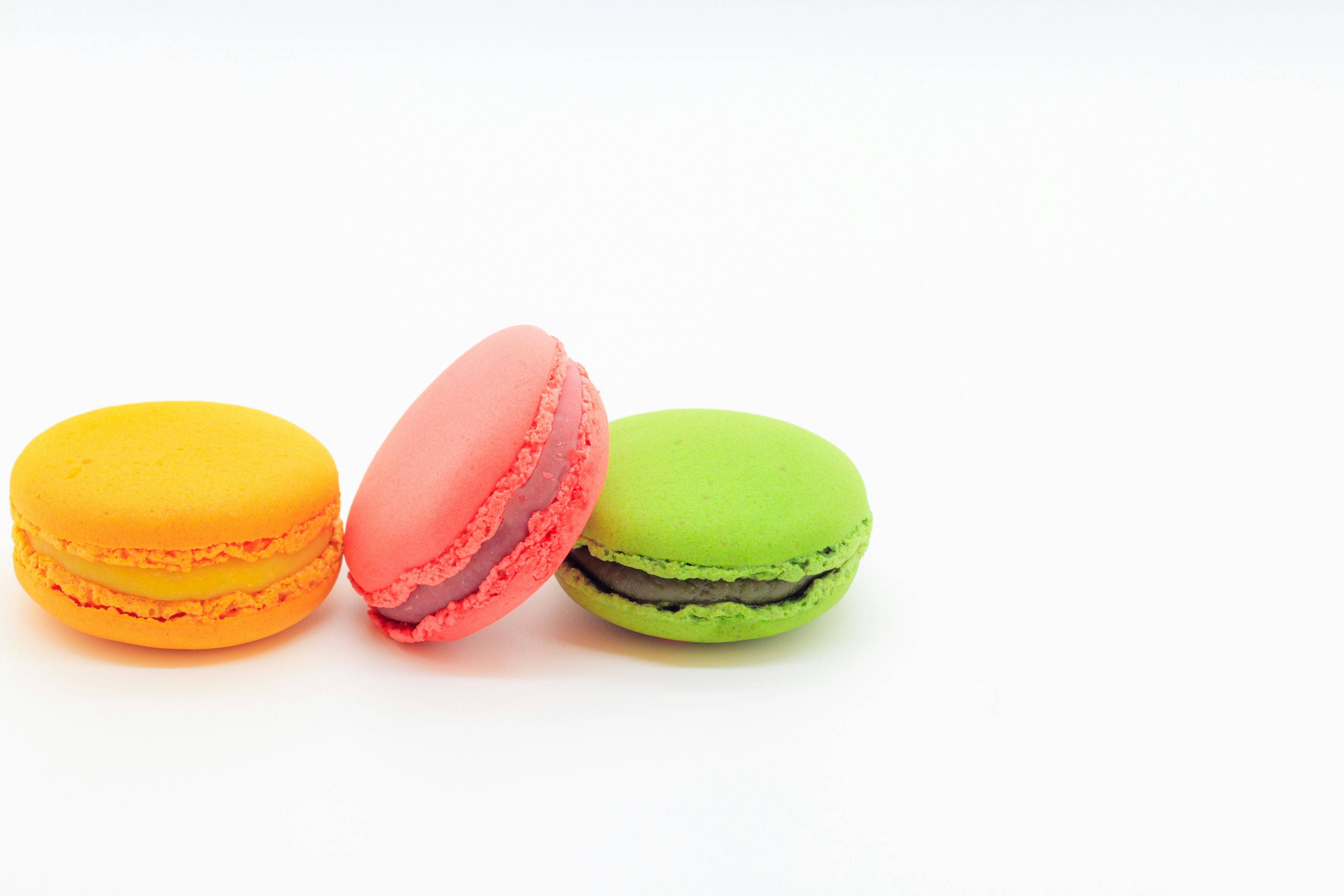 Tres macarons de colores naranja, rosa y verde sobre un fondo simple