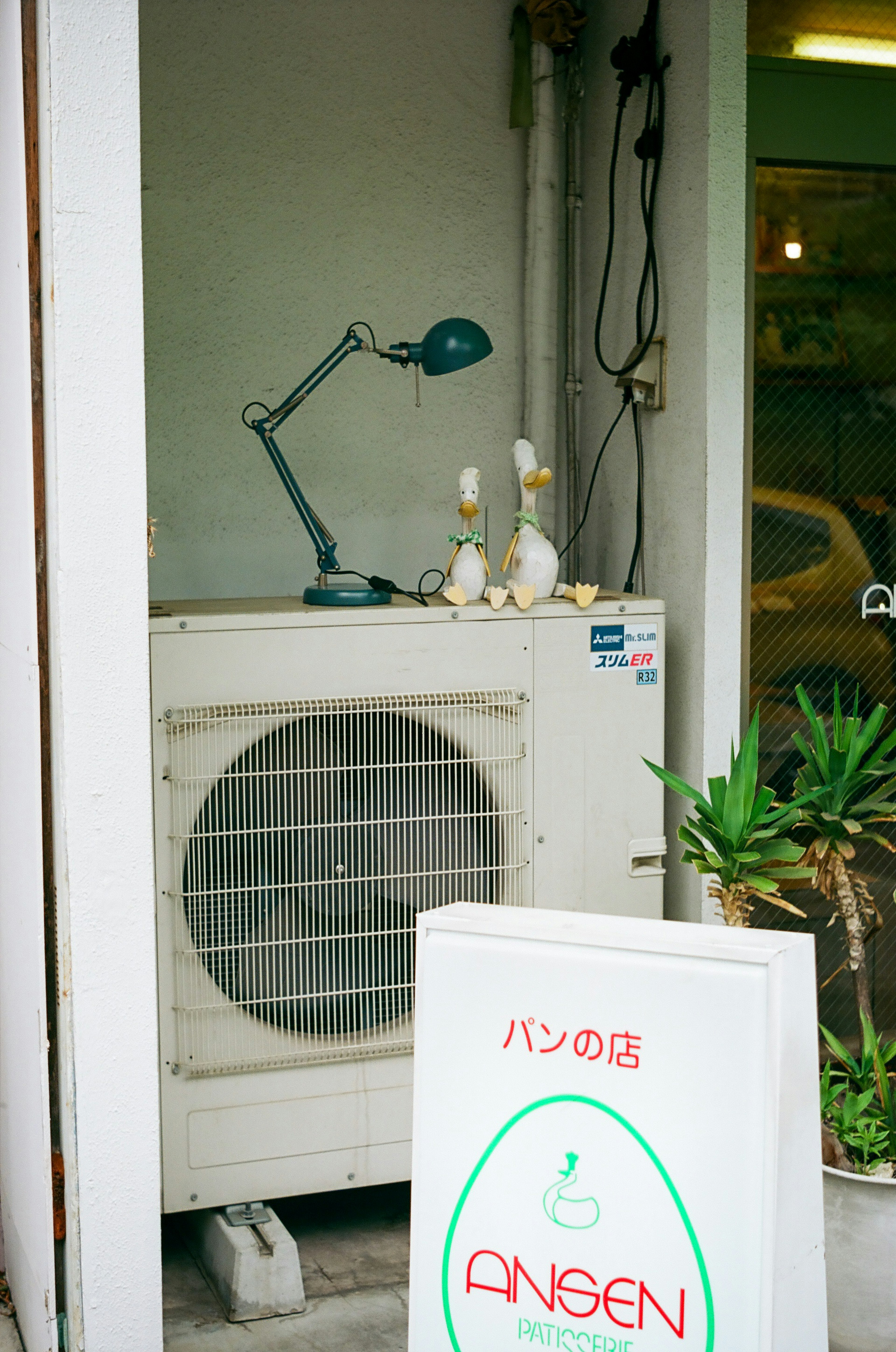 View of an air conditioning unit with a desk lamp and decorative ducks at a shop entrance