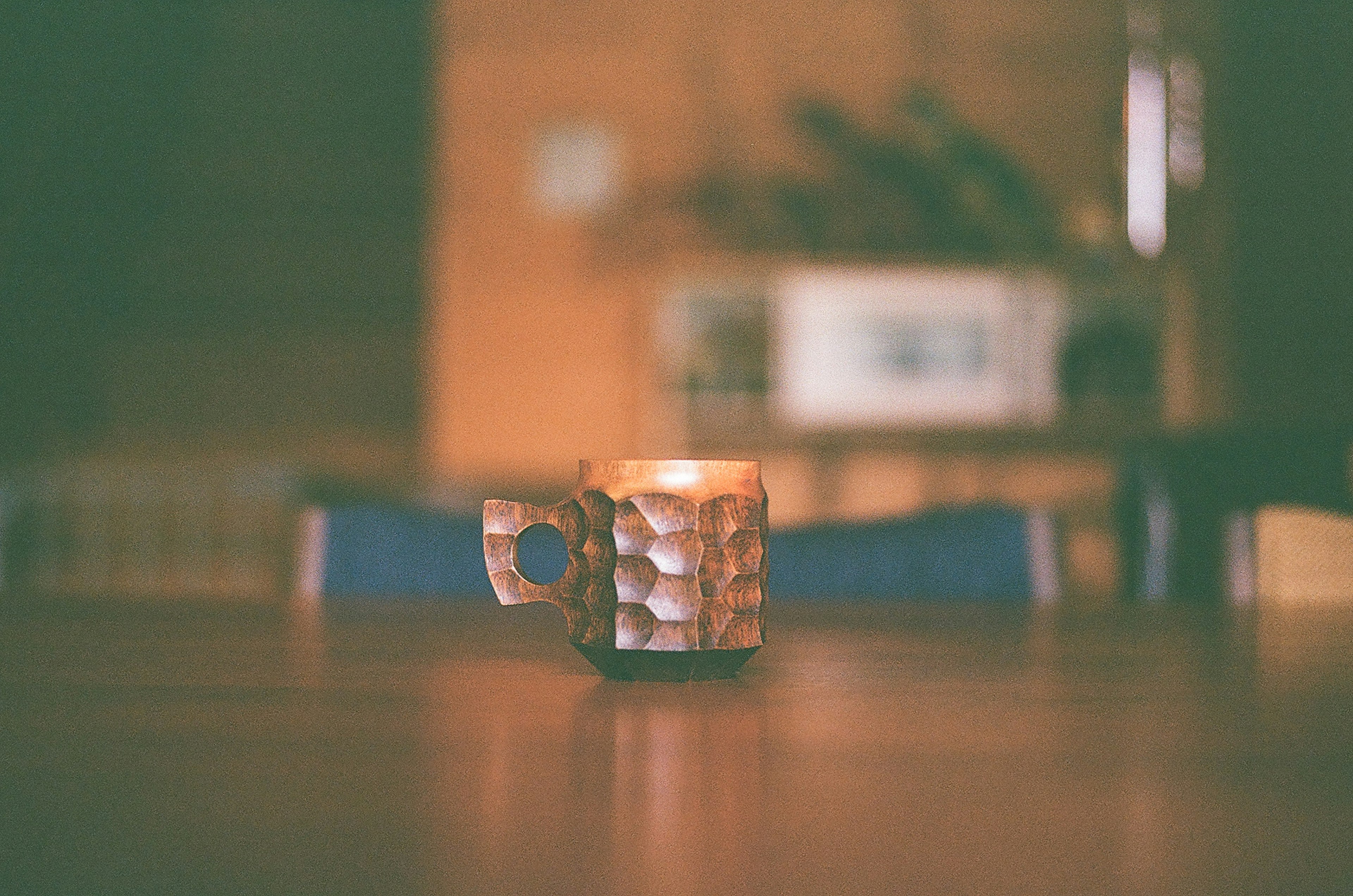 Une bougie dans une tasse texturée sur une table en bois avec un arrière-plan flou de cuisine