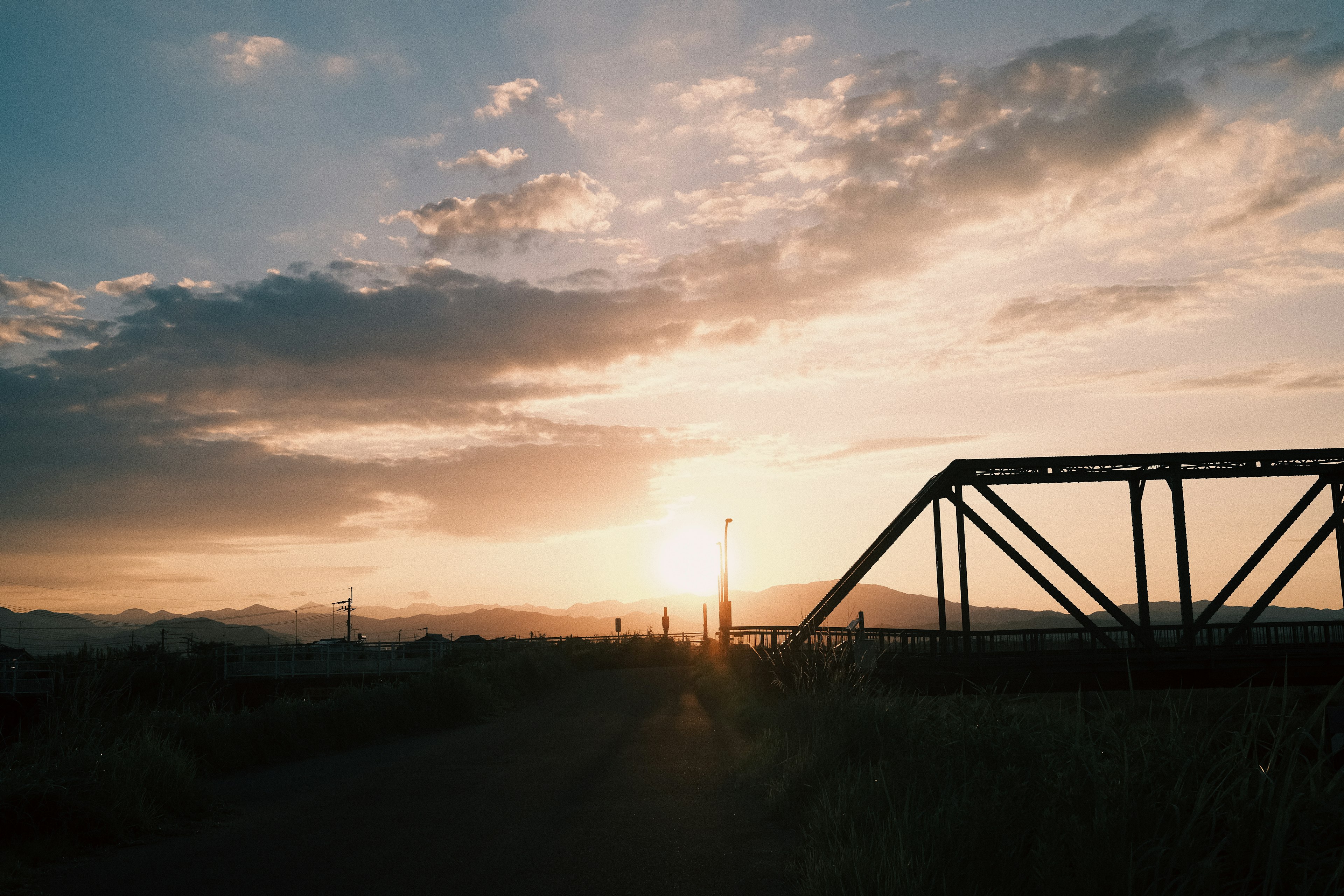 Eisenbahnbrücke vor einem Sonnenuntergang mit grasbewachsenen Feldern