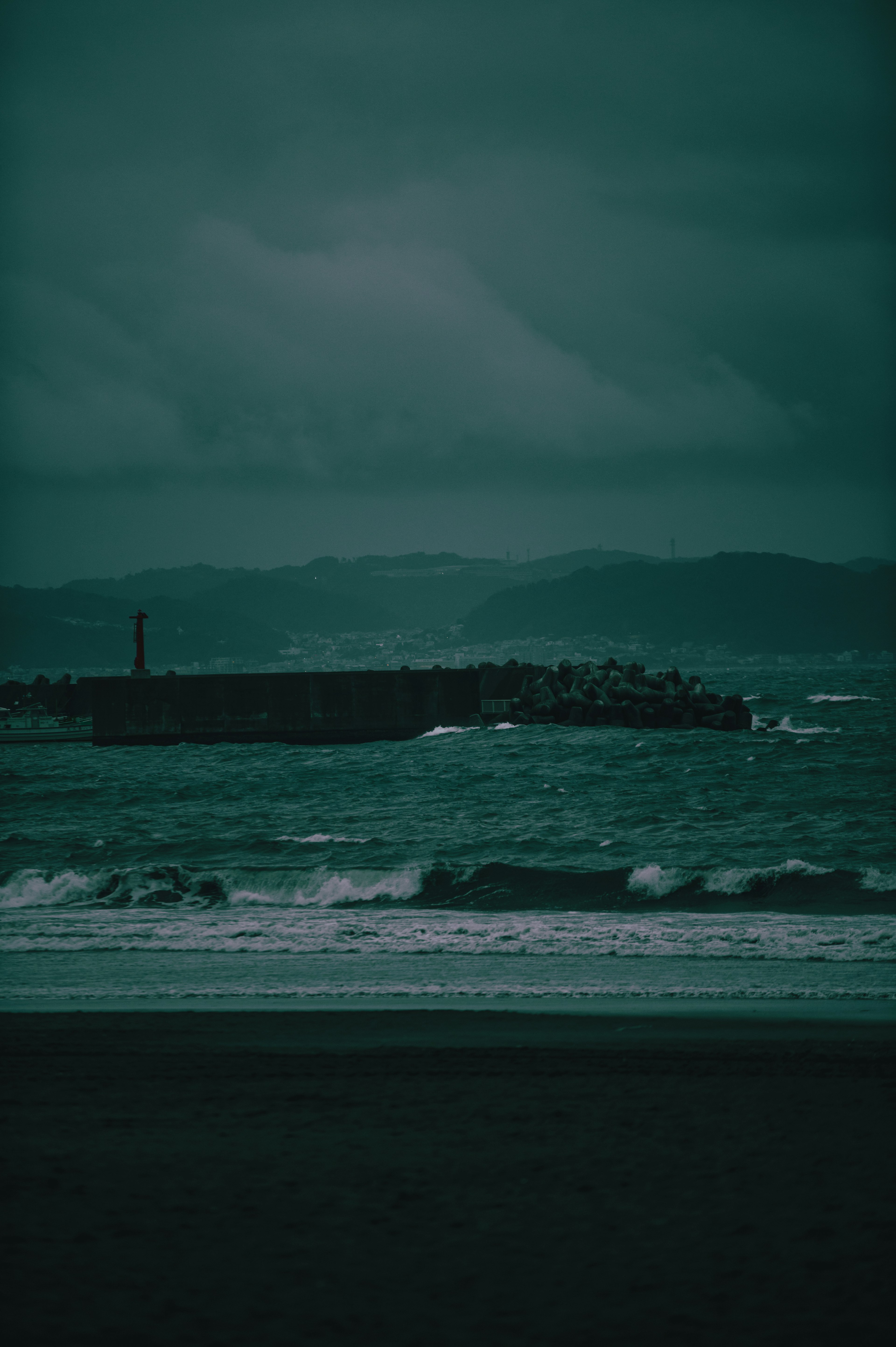 A moody seascape with dark waves and a distant jetty