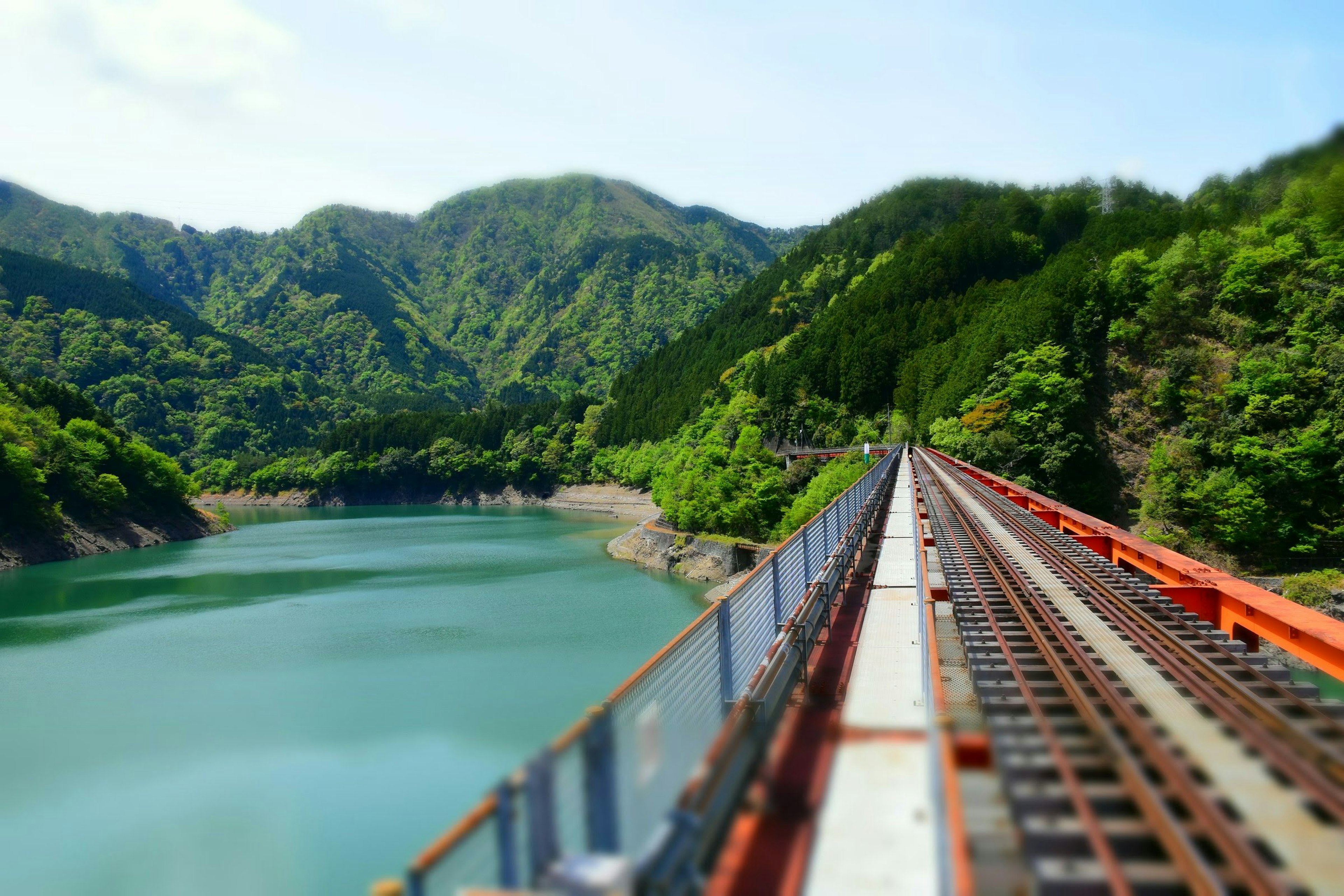 A railway track stretching over a turquoise lake surrounded by lush green mountains