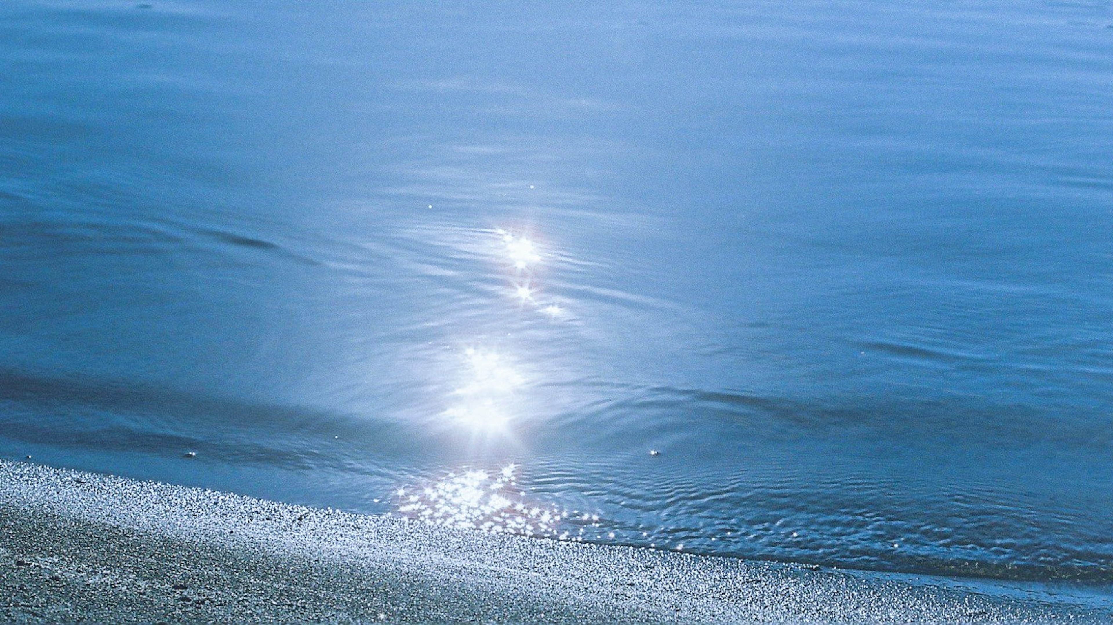 Ruhiger Strand mit Sonnenlicht, das sich auf blauem Wasser spiegelt