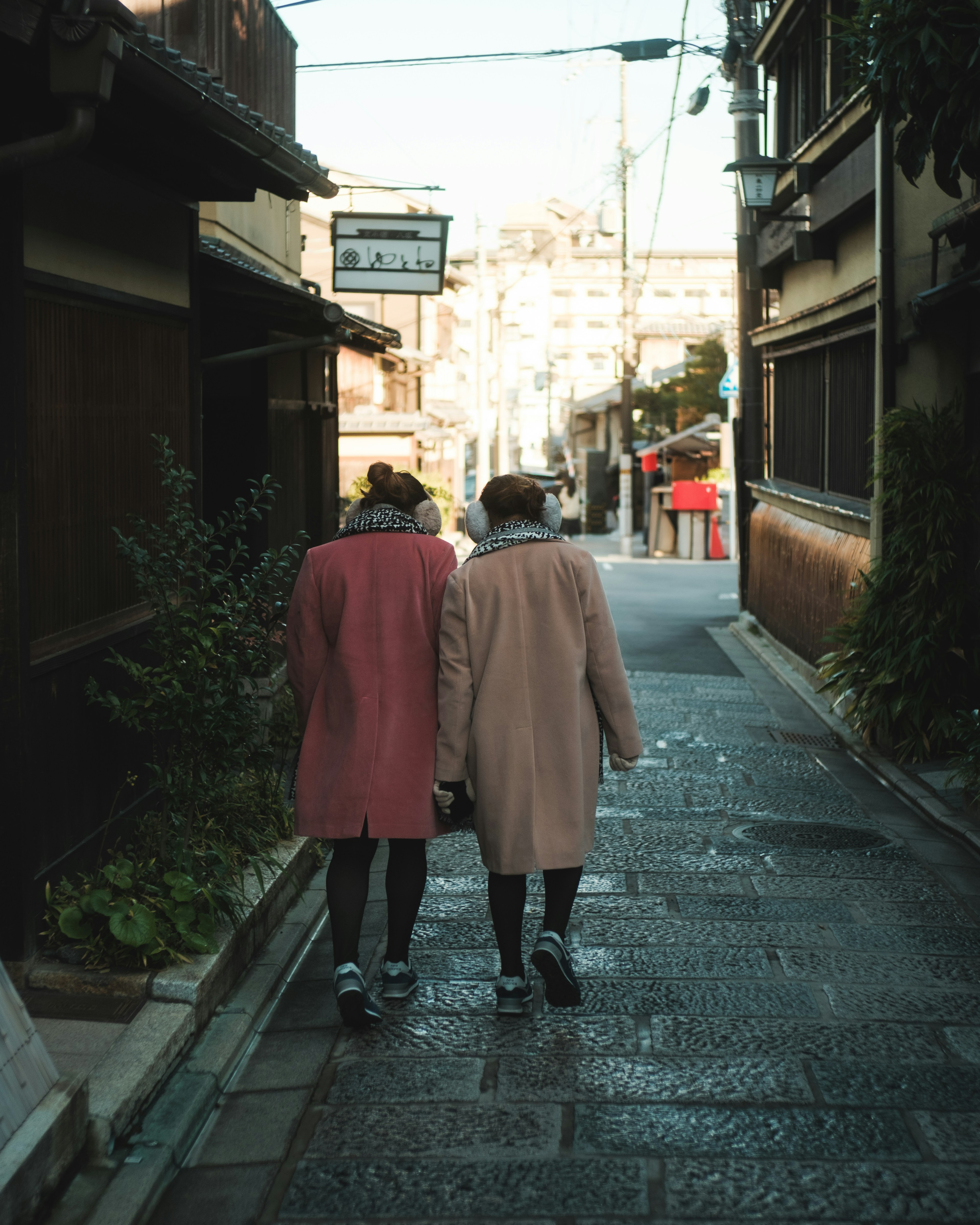 Two women walking down a narrow street wearing pink coats