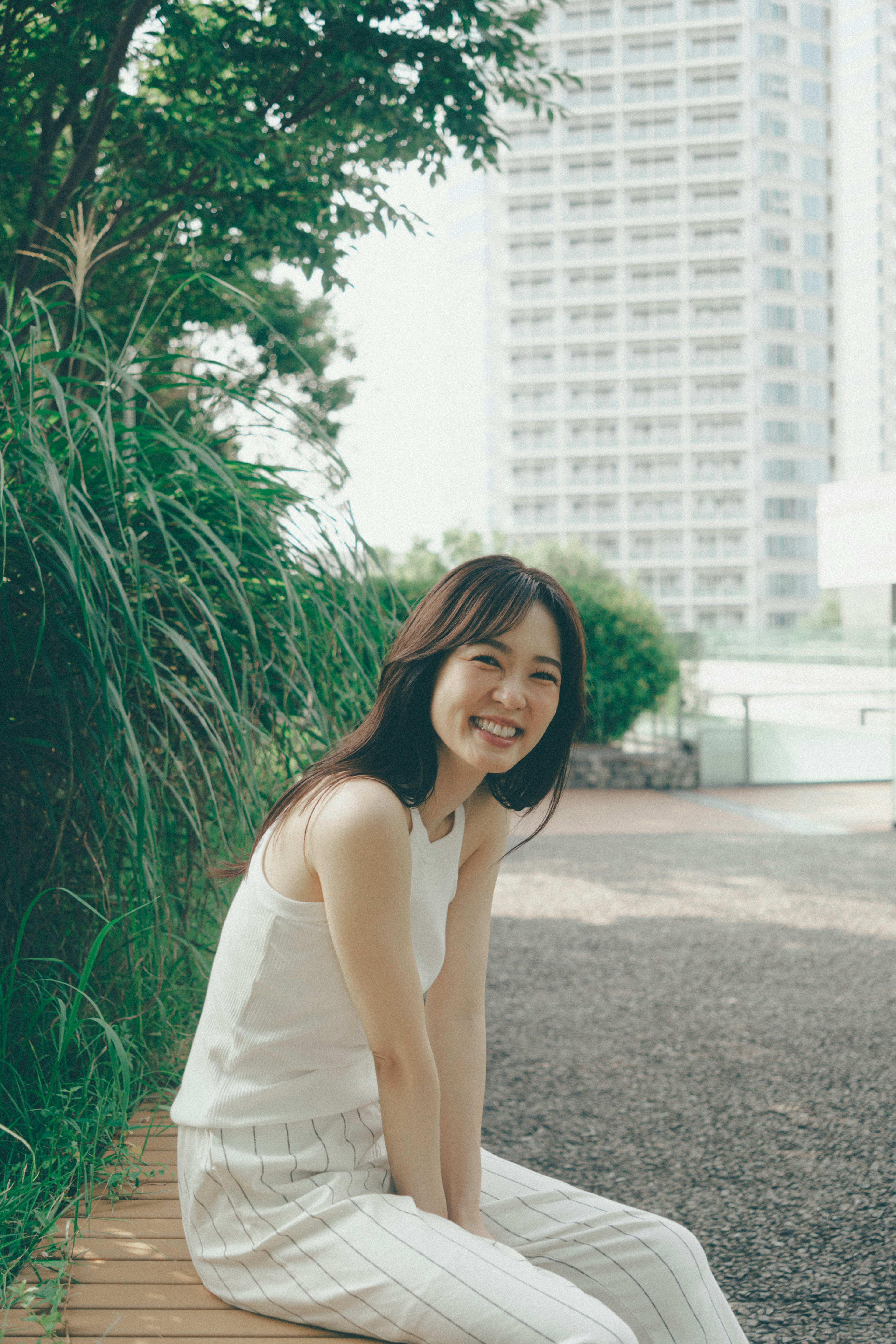 A smiling woman sitting in a park surrounded by greenery