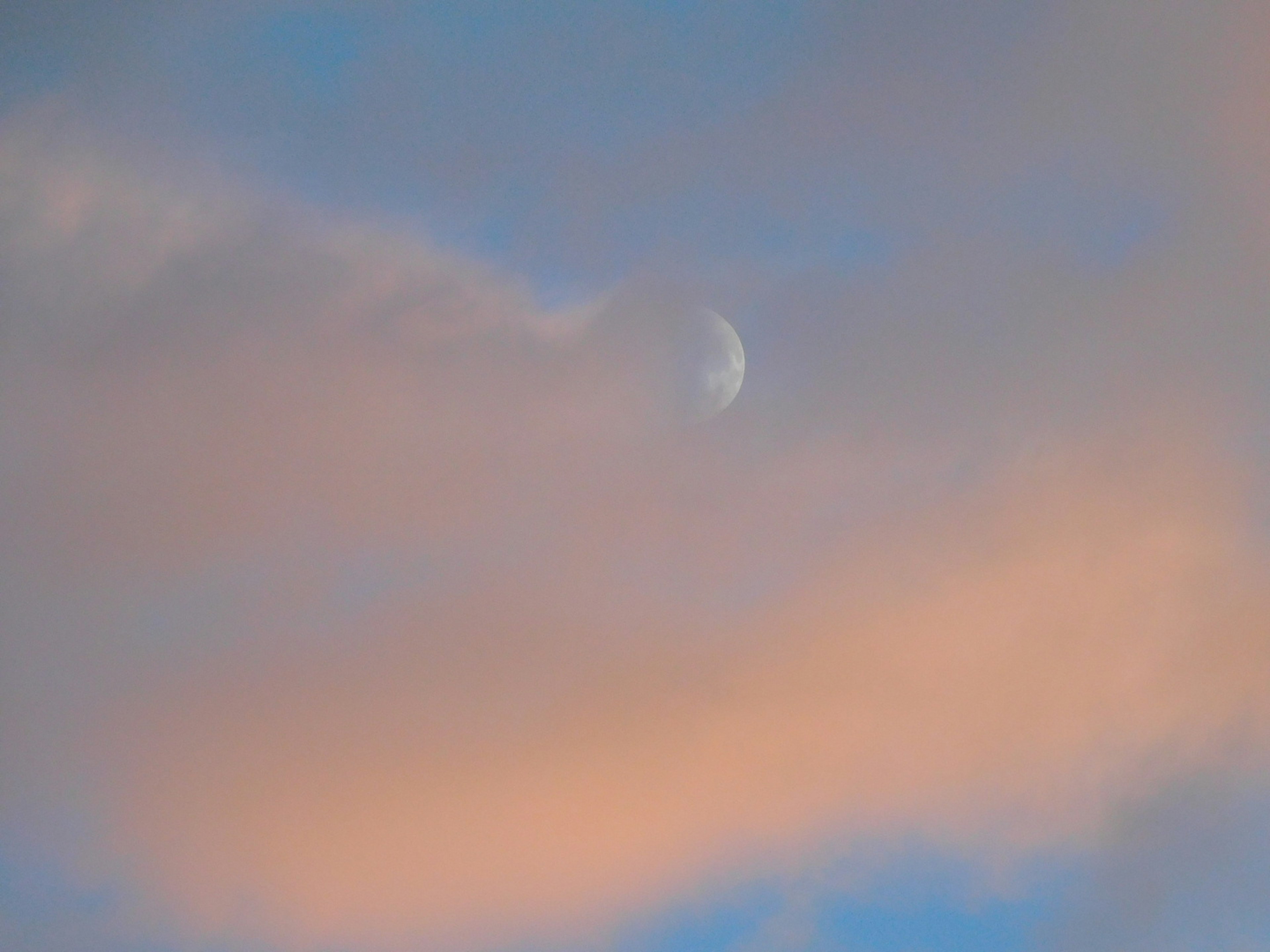 Luna parzialmente visibile tra nuvole morbide in un cielo blu