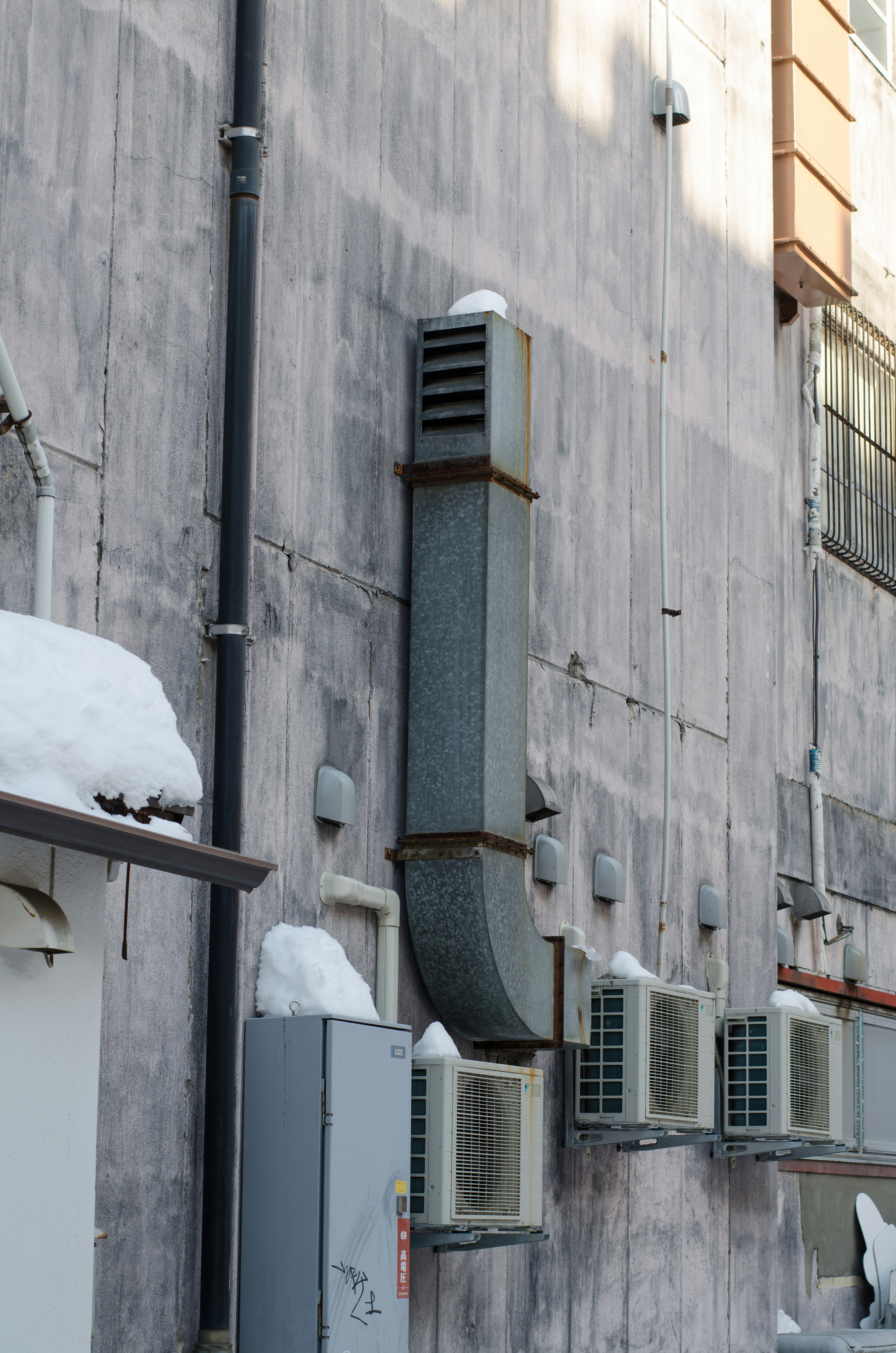 Air conditioning units and ventilation duct on a snow-covered wall