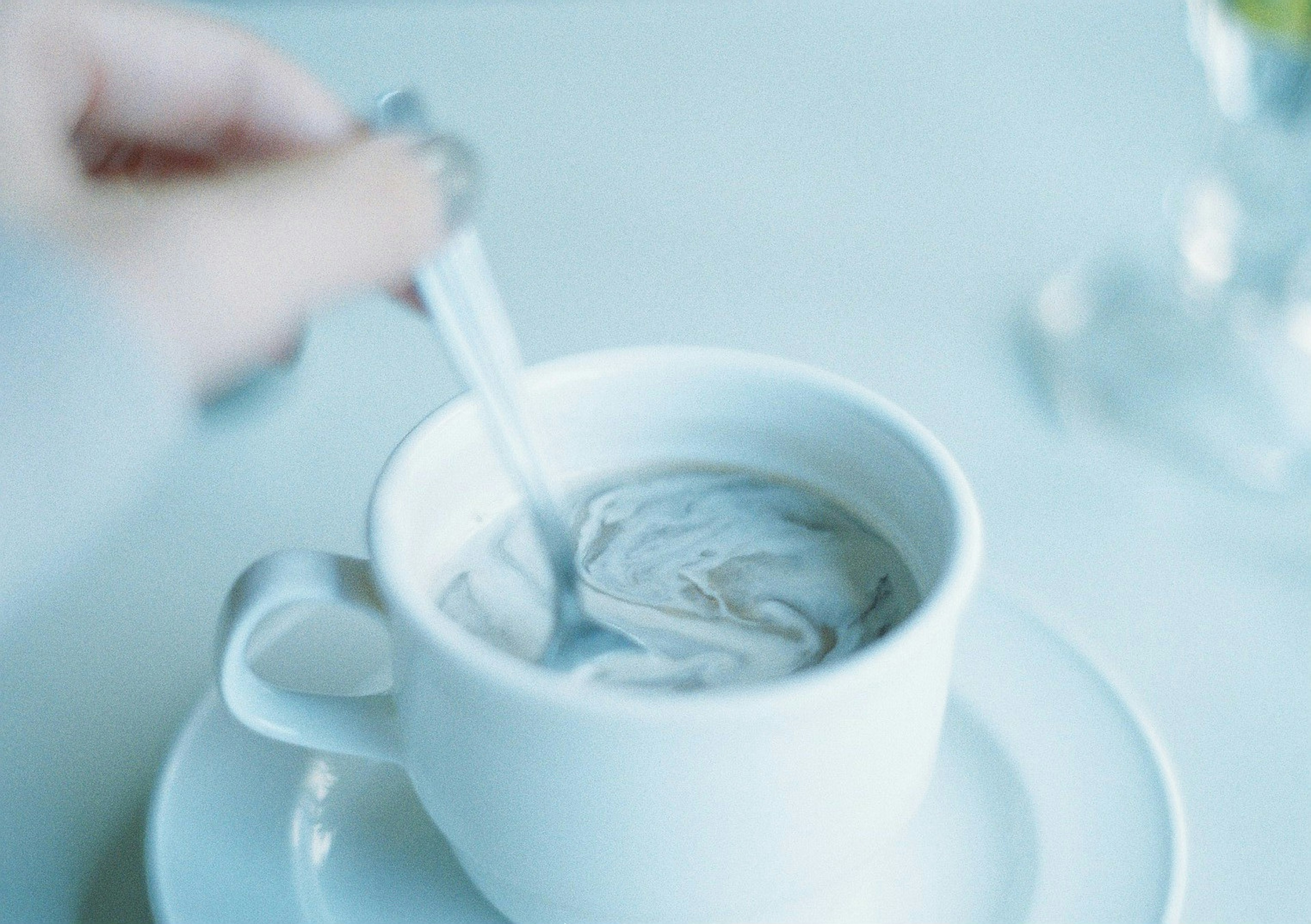 Main en train de remuer du café dans une tasse blanche