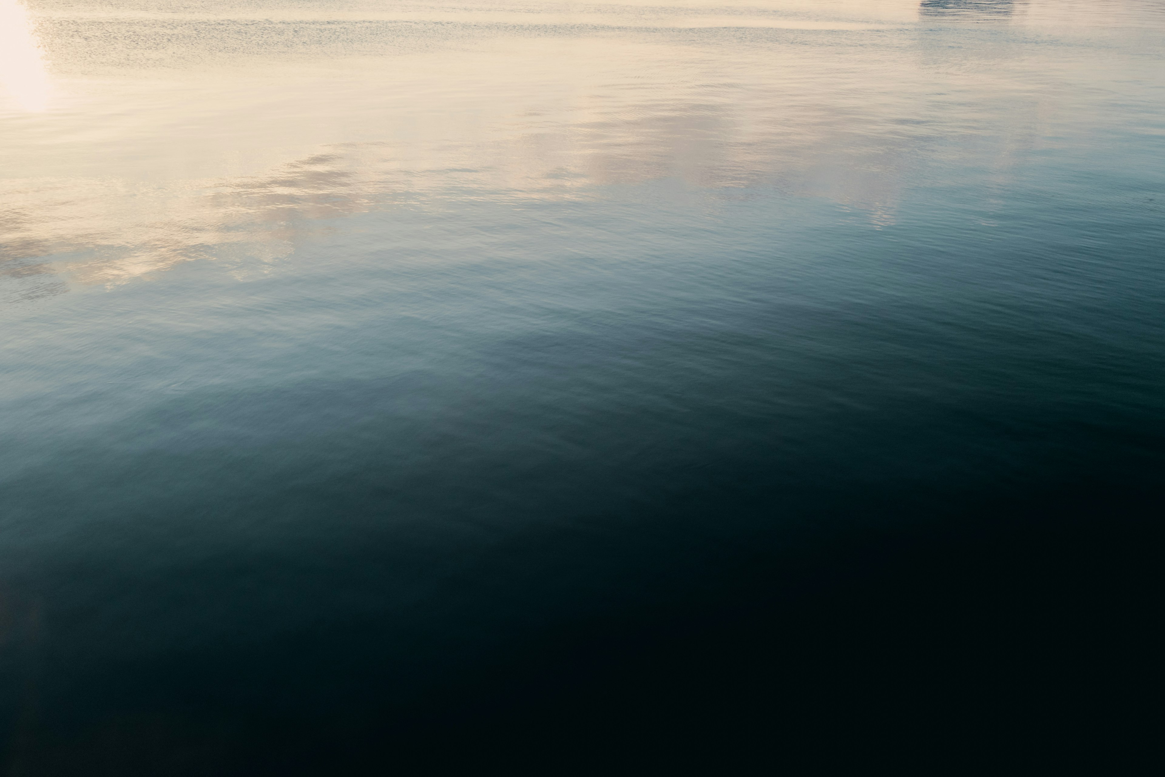 Superficie d'acqua calma che riflette una luce morbida e nuvole