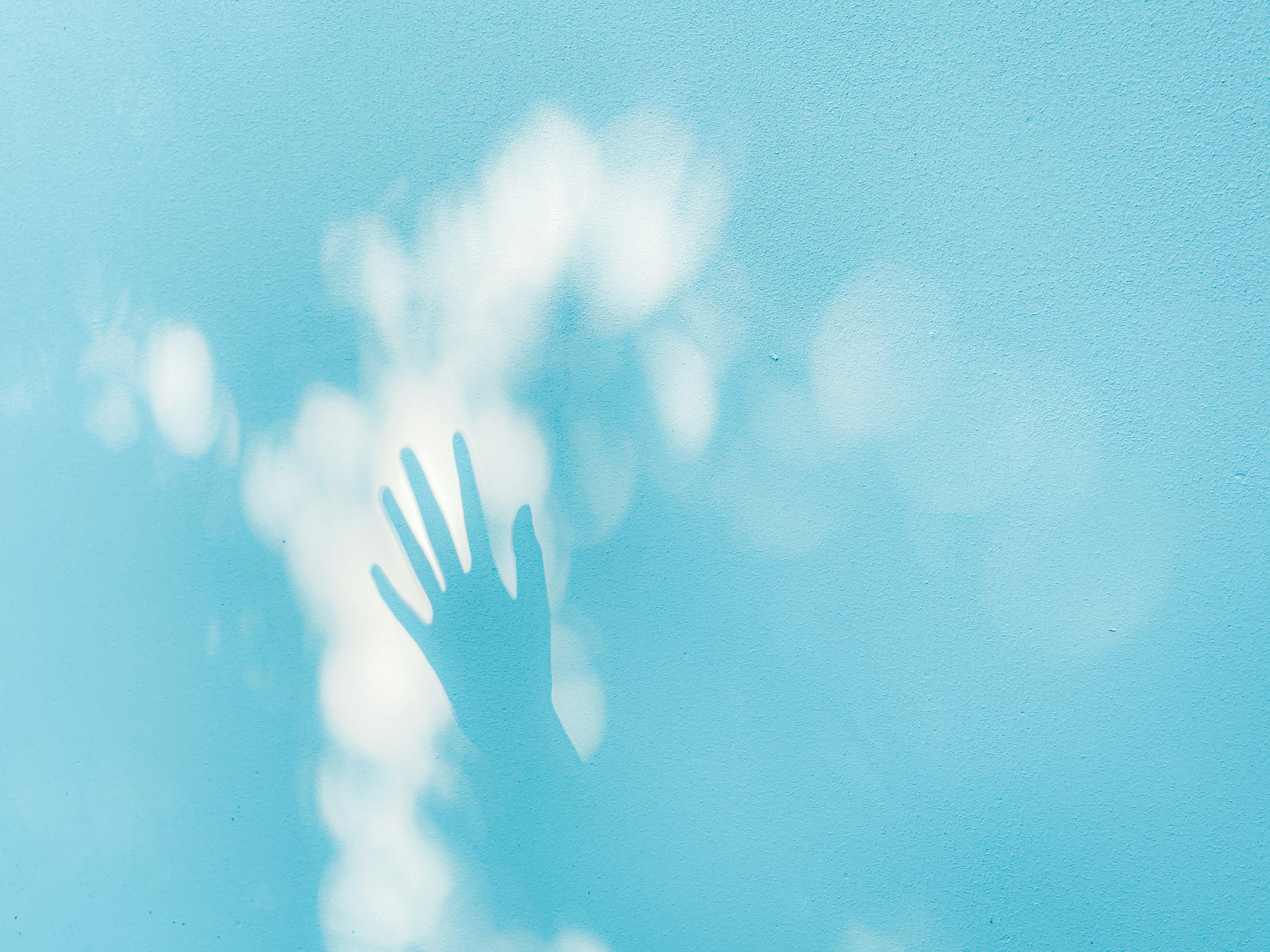 Shadow of a hand against a blue background with soft clouds