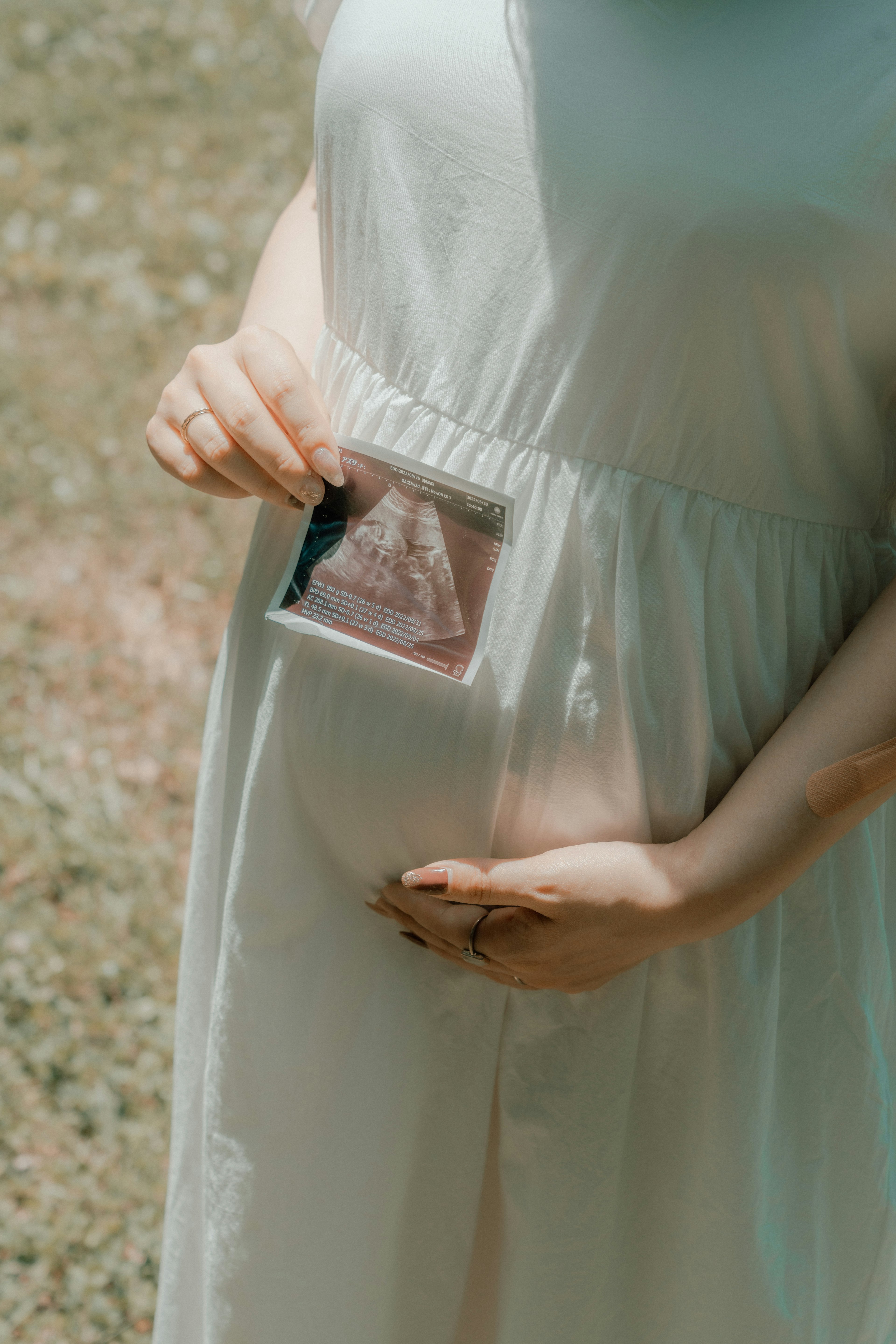 Donna incinta in abito bianco tiene una foto dell'ecografia contro il suo pancione