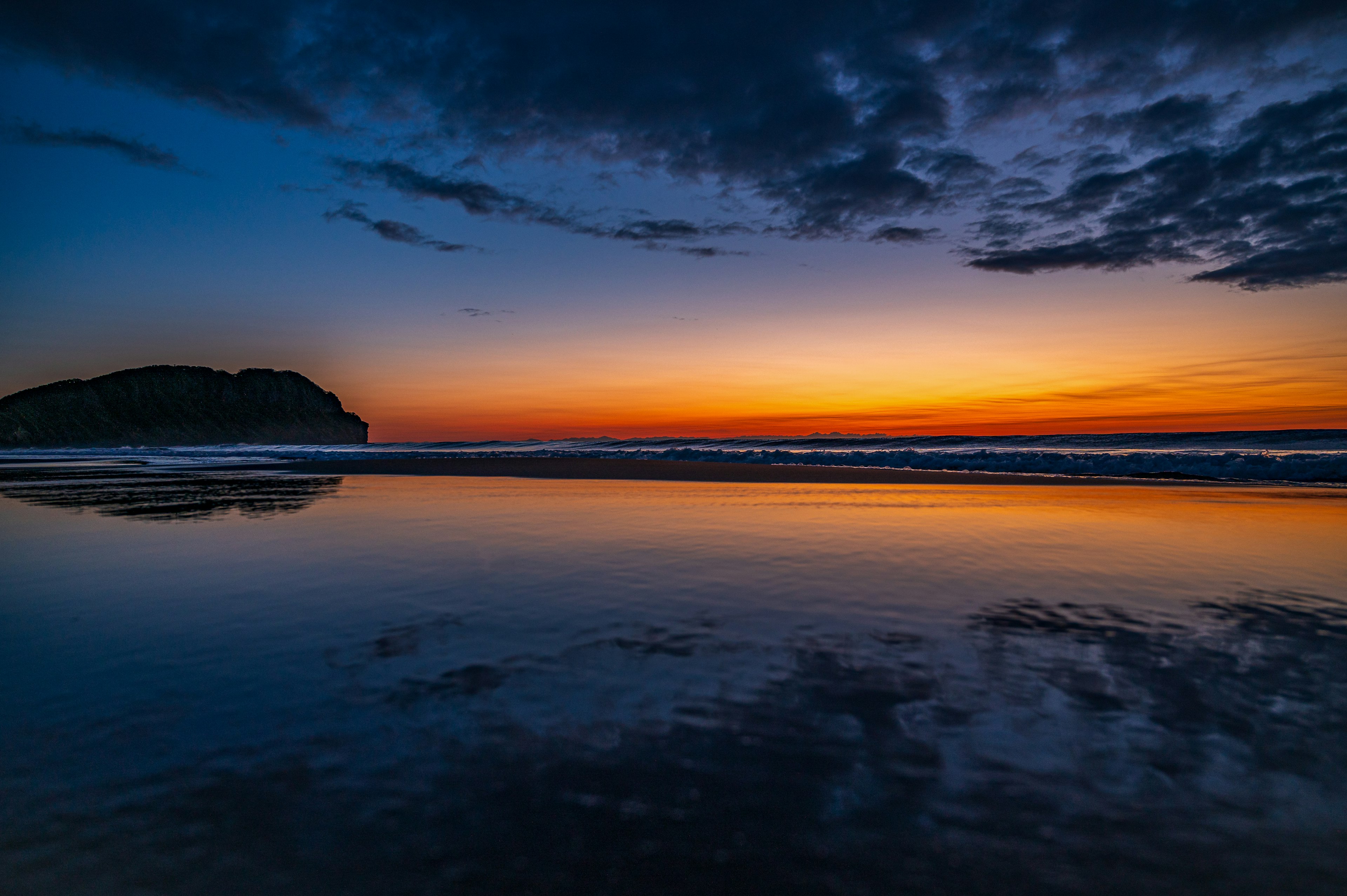 美しい夕焼けの海岸の風景 水面に映る夕焼けの色合い 岩のシルエット