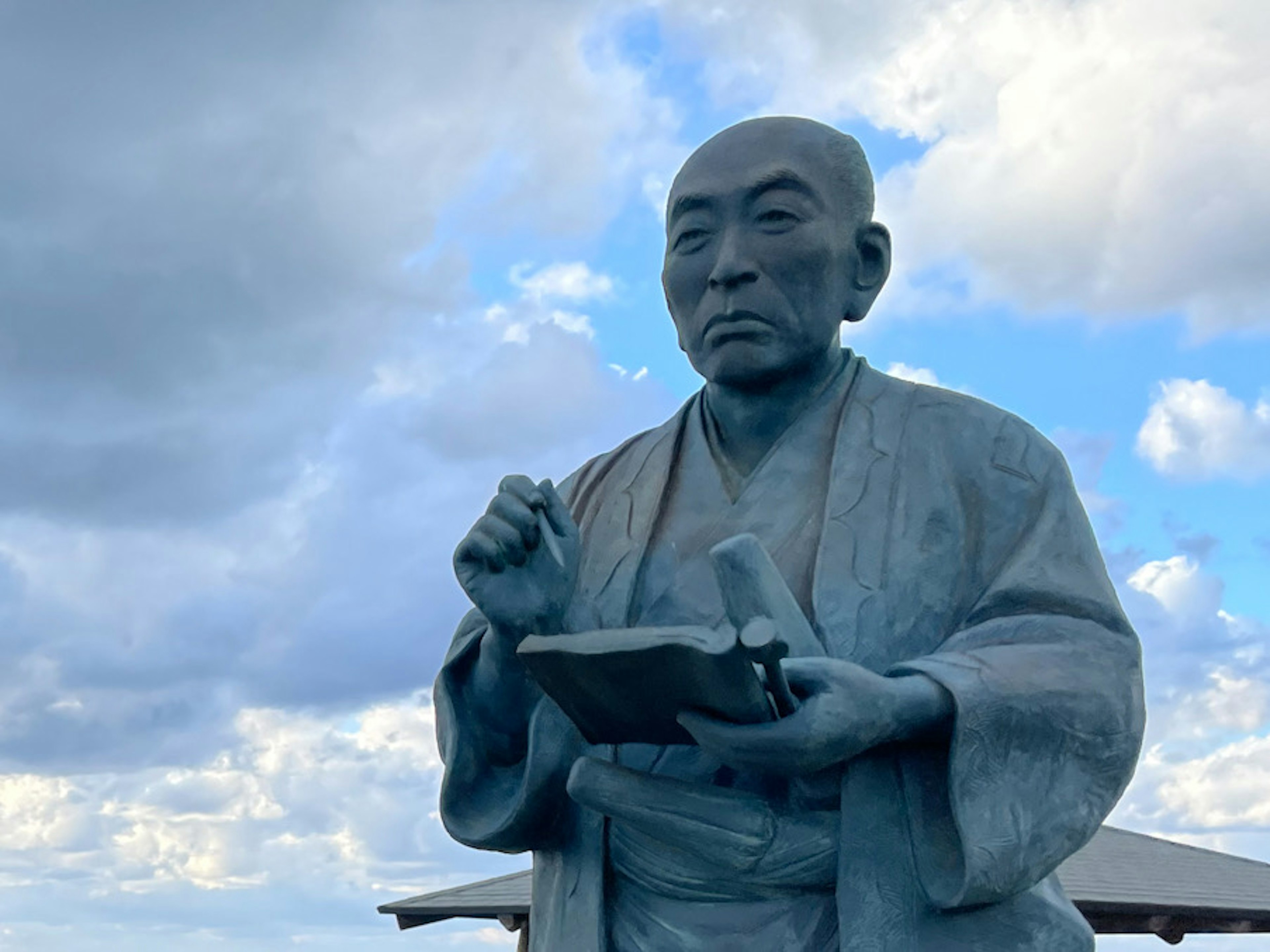 青空の下に立つ書物を持つ石像の男性