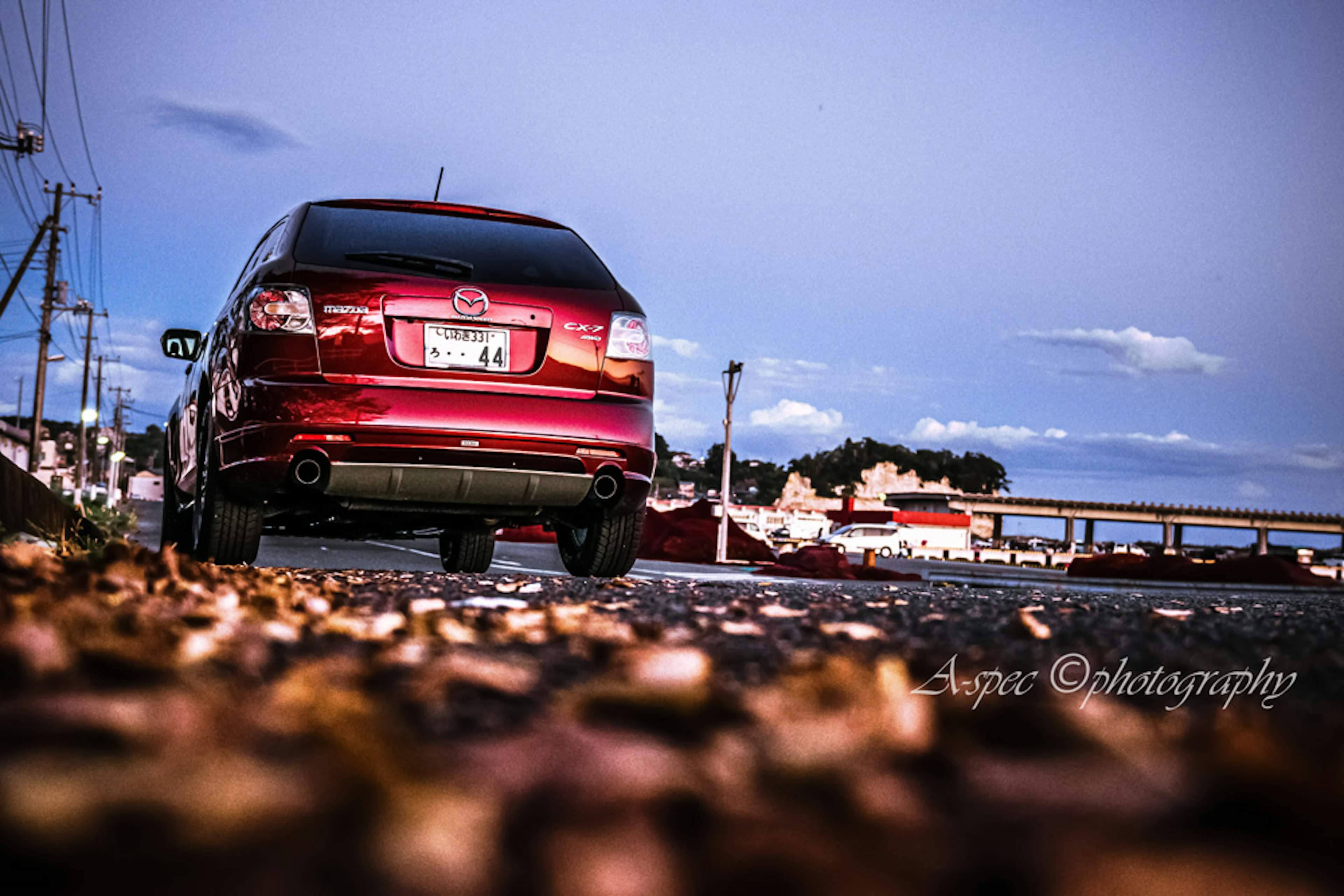 A red car parked on a leaf-covered road with a scenic backdrop