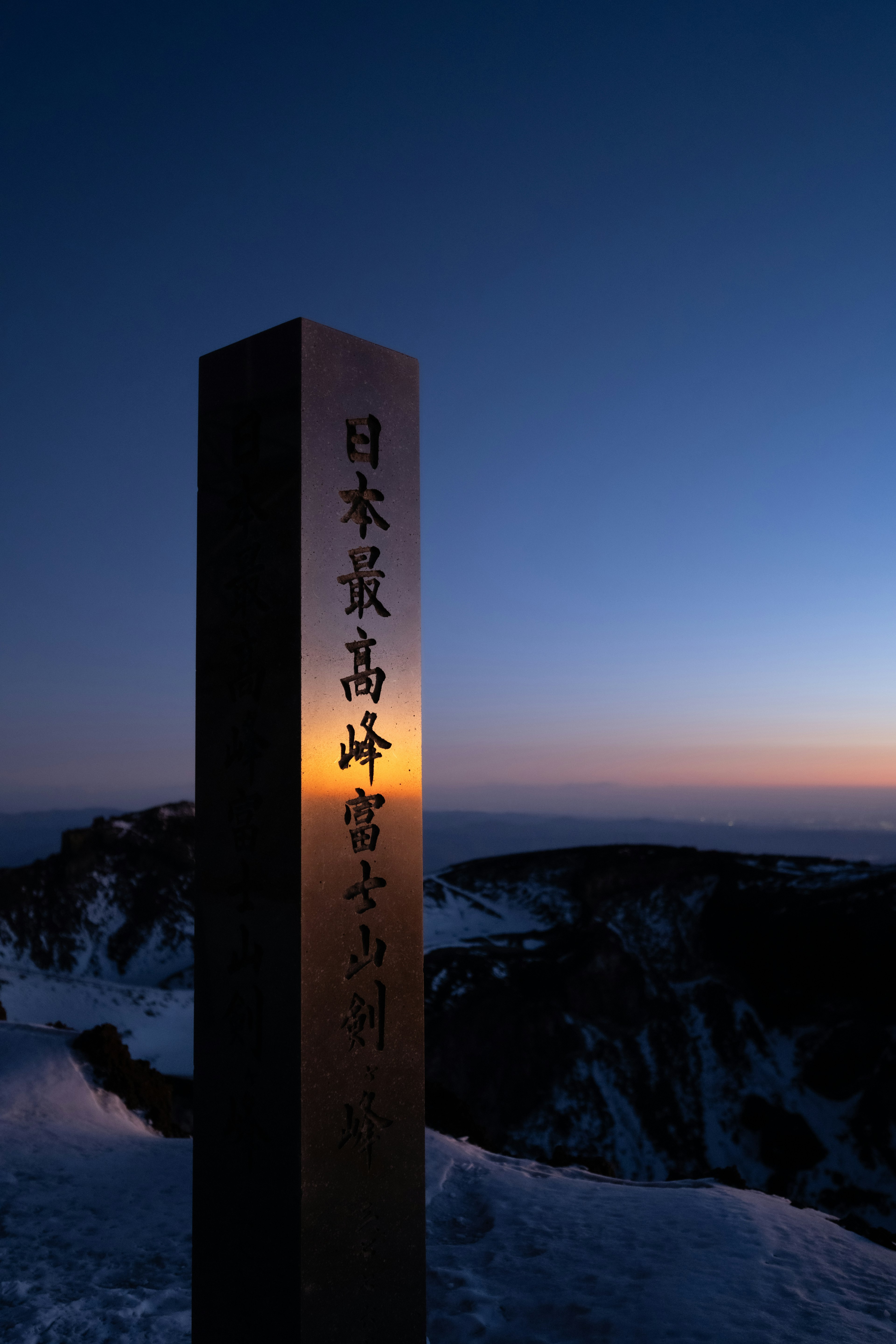 山頂に立つ標識が夕日の光を受けて輝いている風景