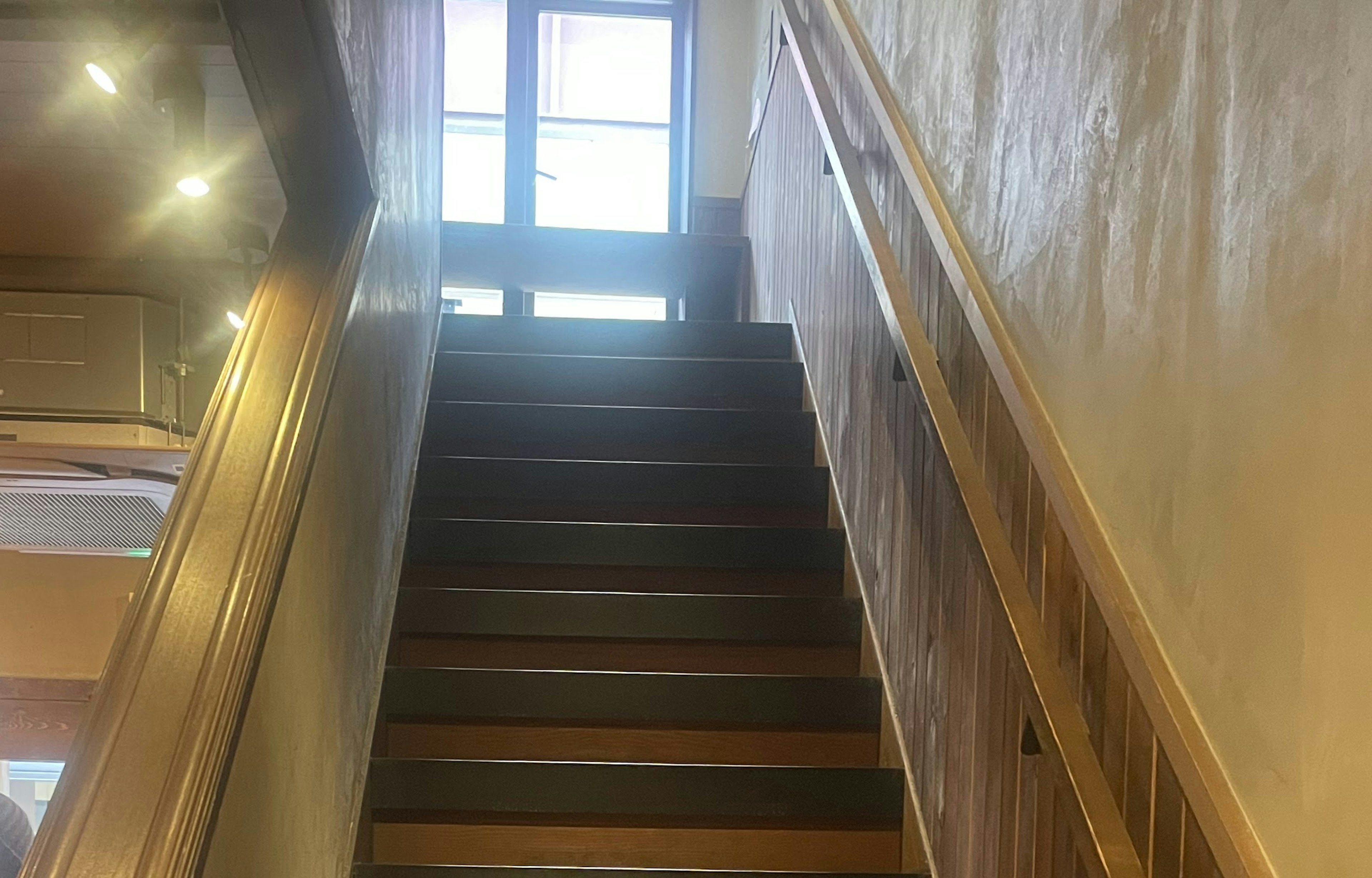 Interior photo of stairs leading to a door with bright windows