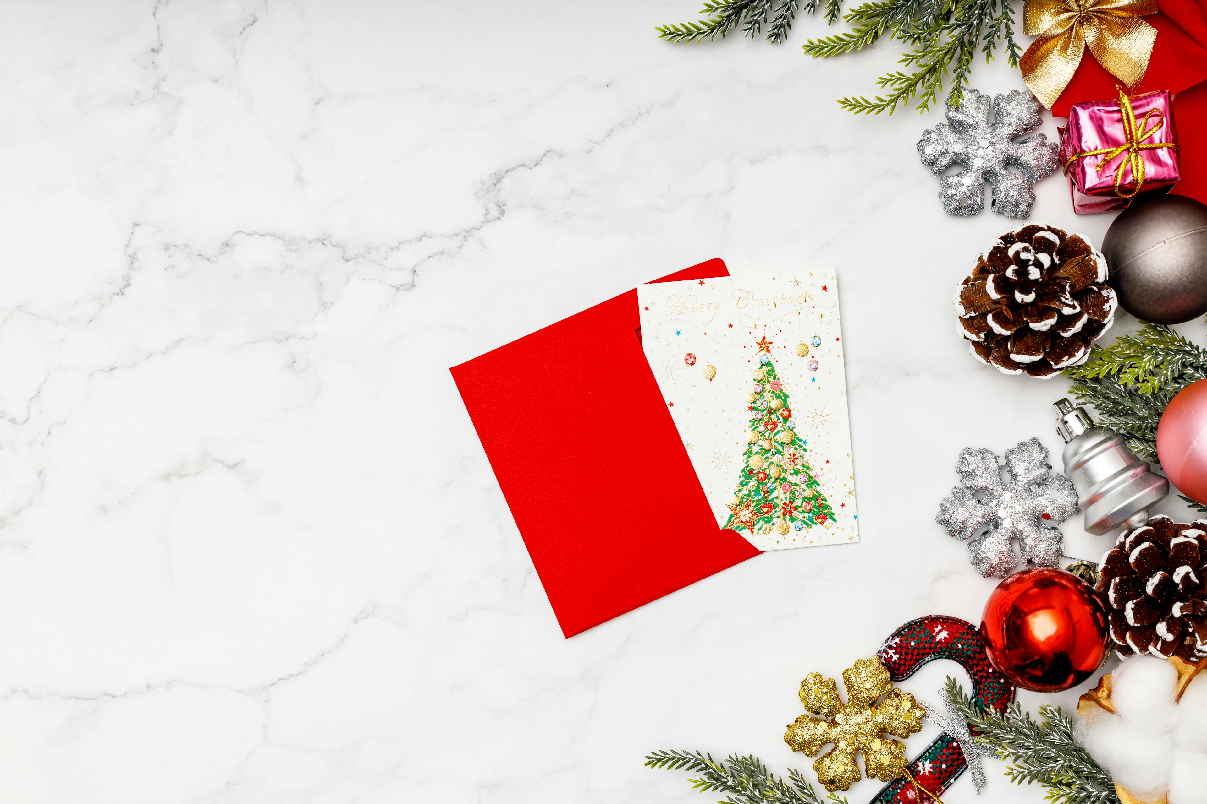 Red envelope with a Christmas tree illustration card surrounded by Christmas decorations and pine cones