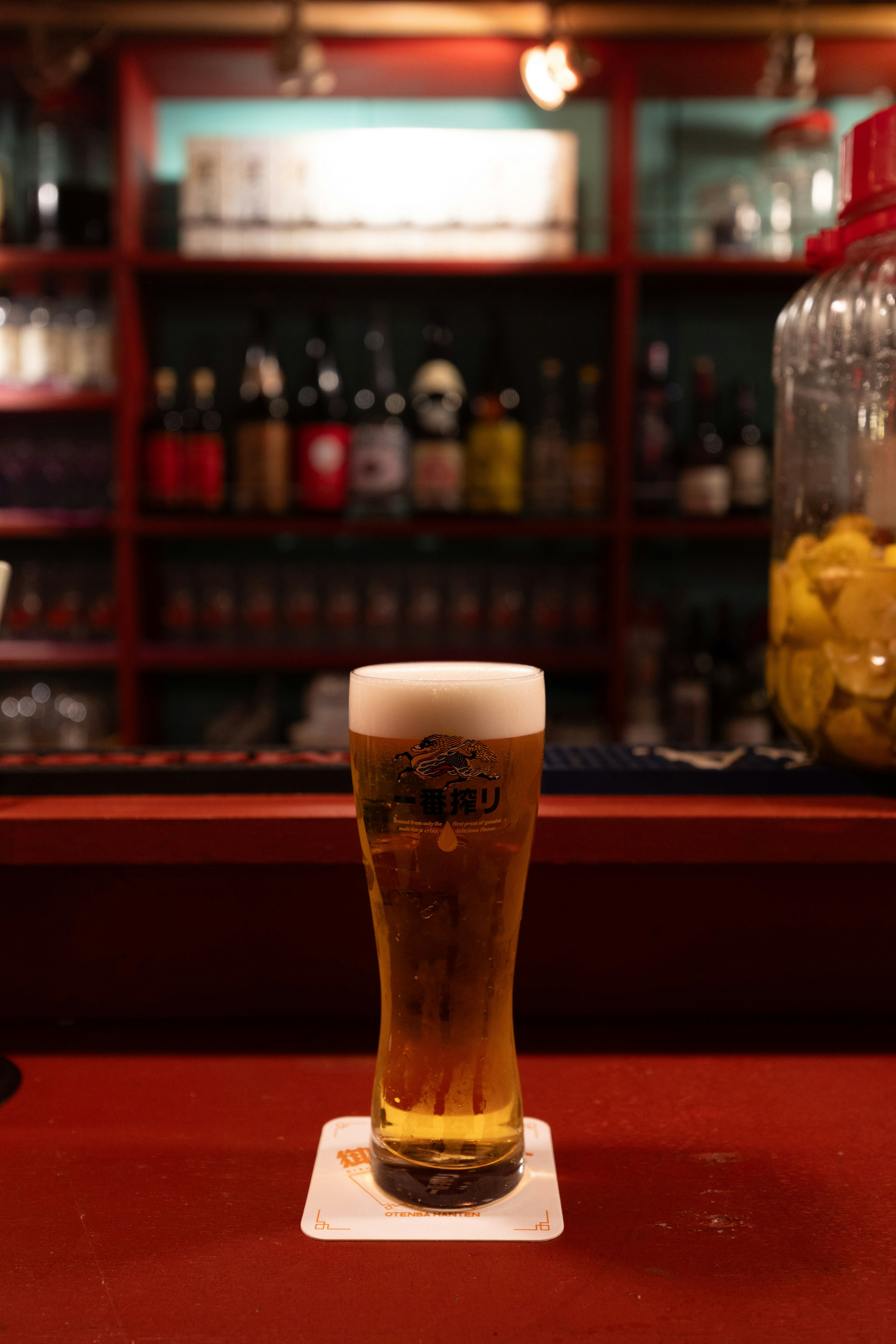 ビールが注がれたグラスがカウンターに置かれた背景には多くのボトルが並ぶバーの内部