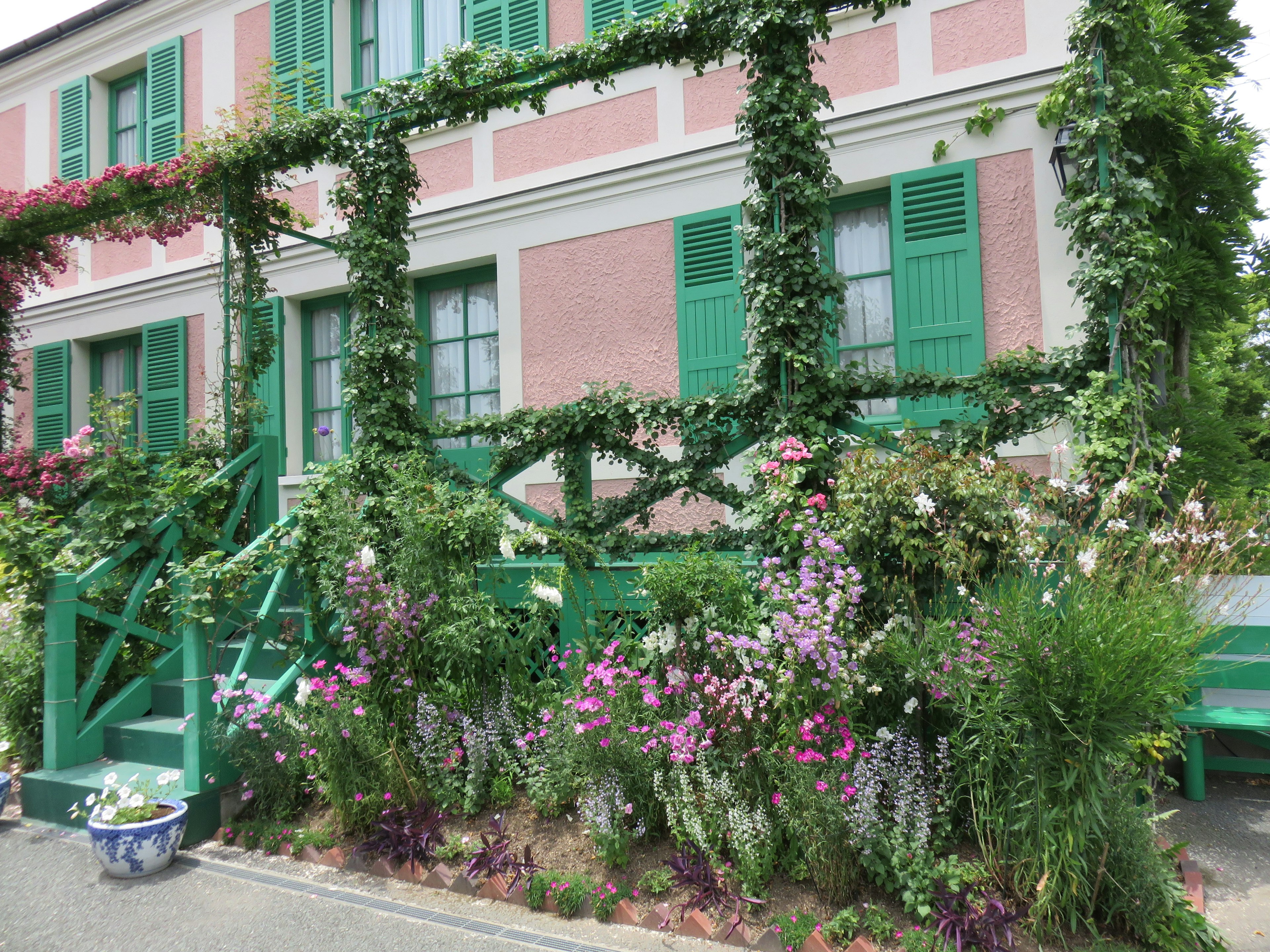 Pink house with green doors and windows surrounded by colorful flowers