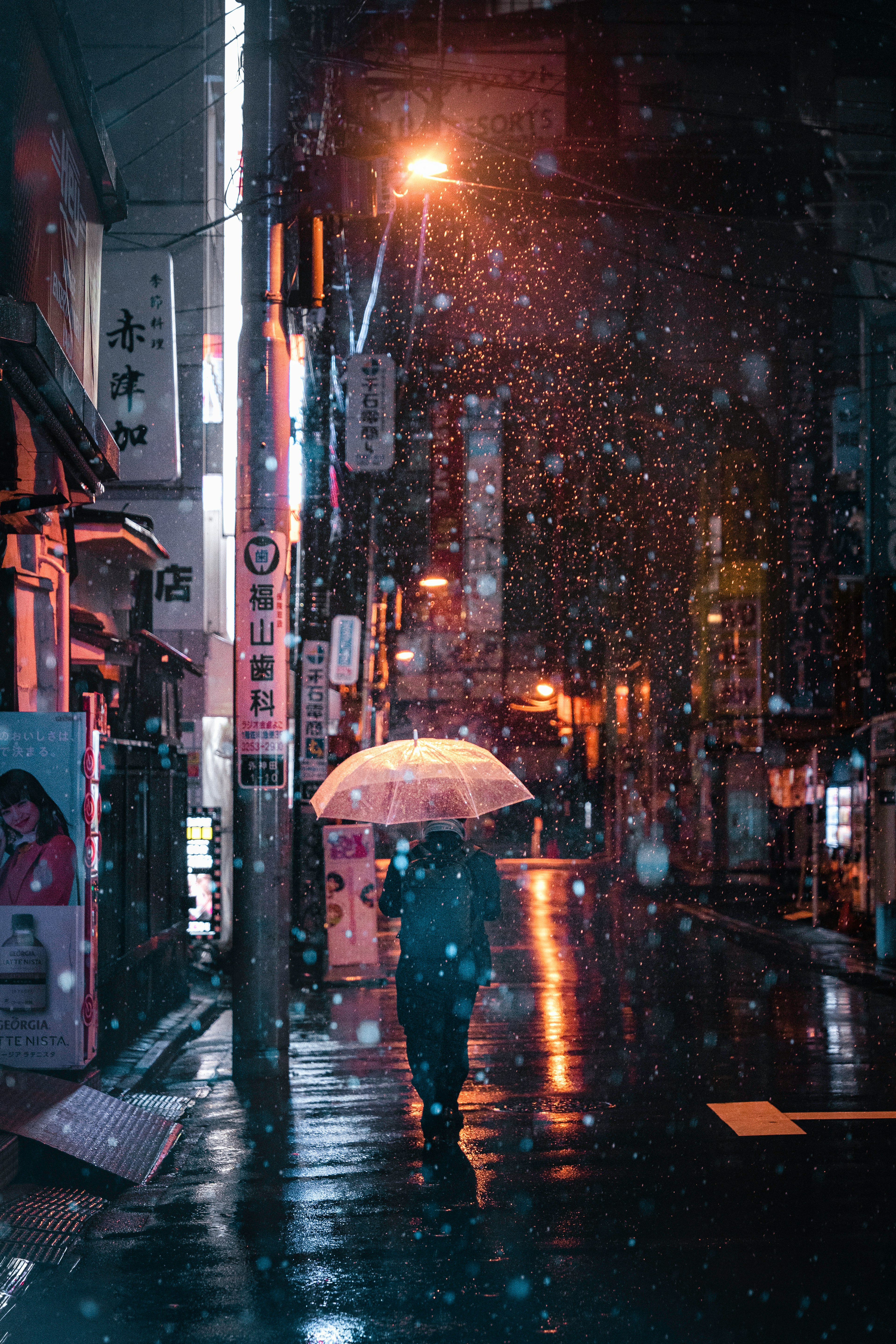 雨の中で傘を差して歩く人物 明るい街灯と色とりどりの看板が映える夜の街