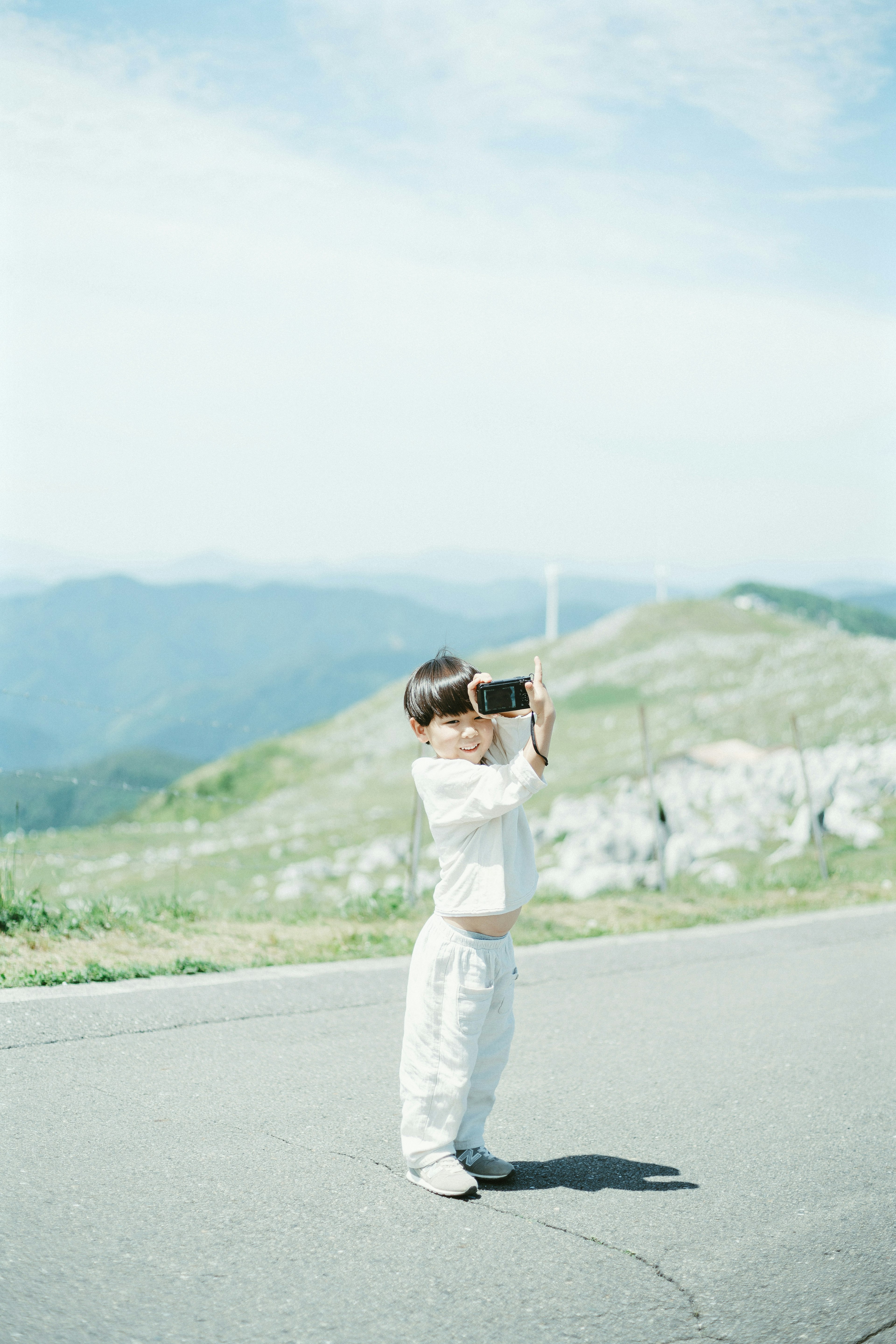 Child holding a camera against a mountainous backdrop