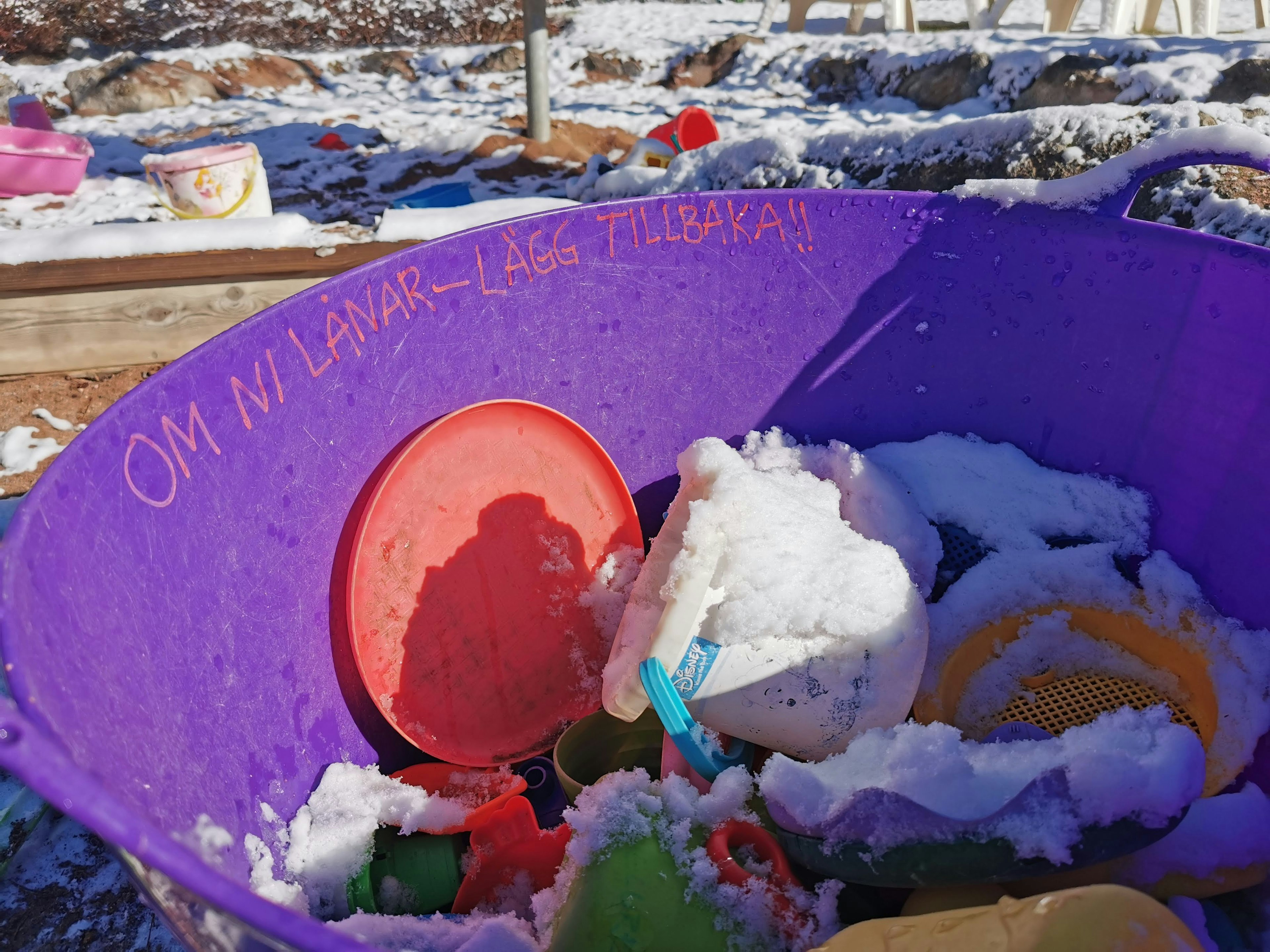 Lila Eimer voller mit Schnee bedeckter Spielzeuge und Plastikgeschirr