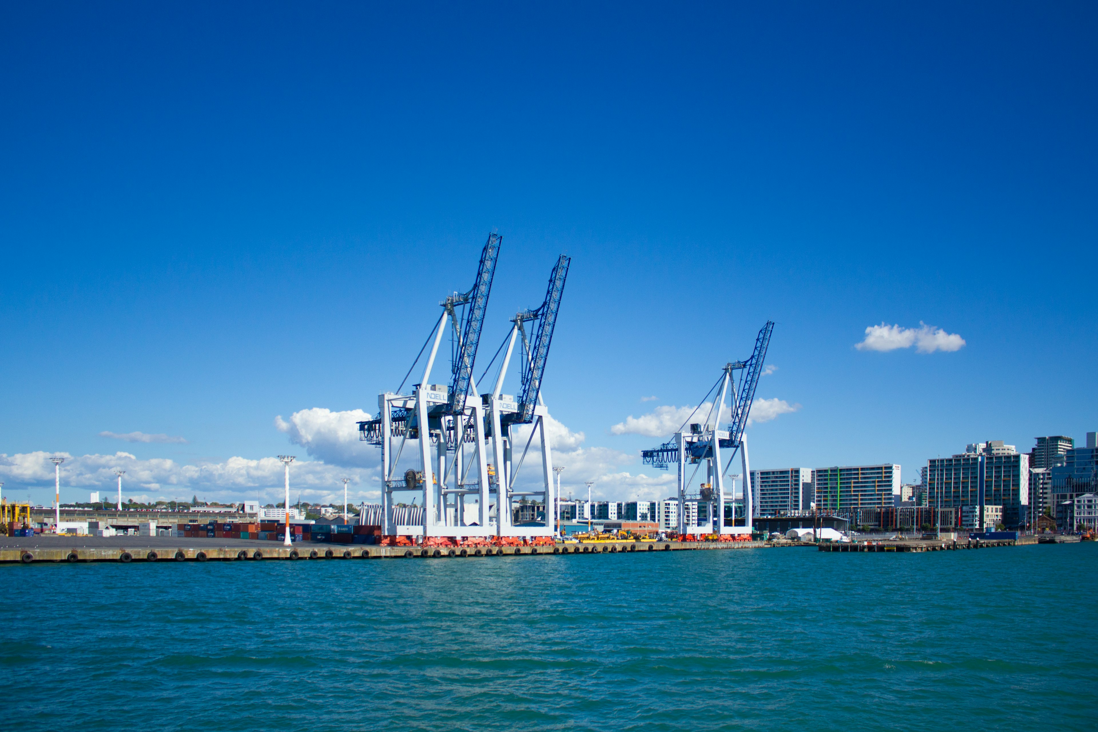 Port cranes standing against a clear blue sky and turquoise water