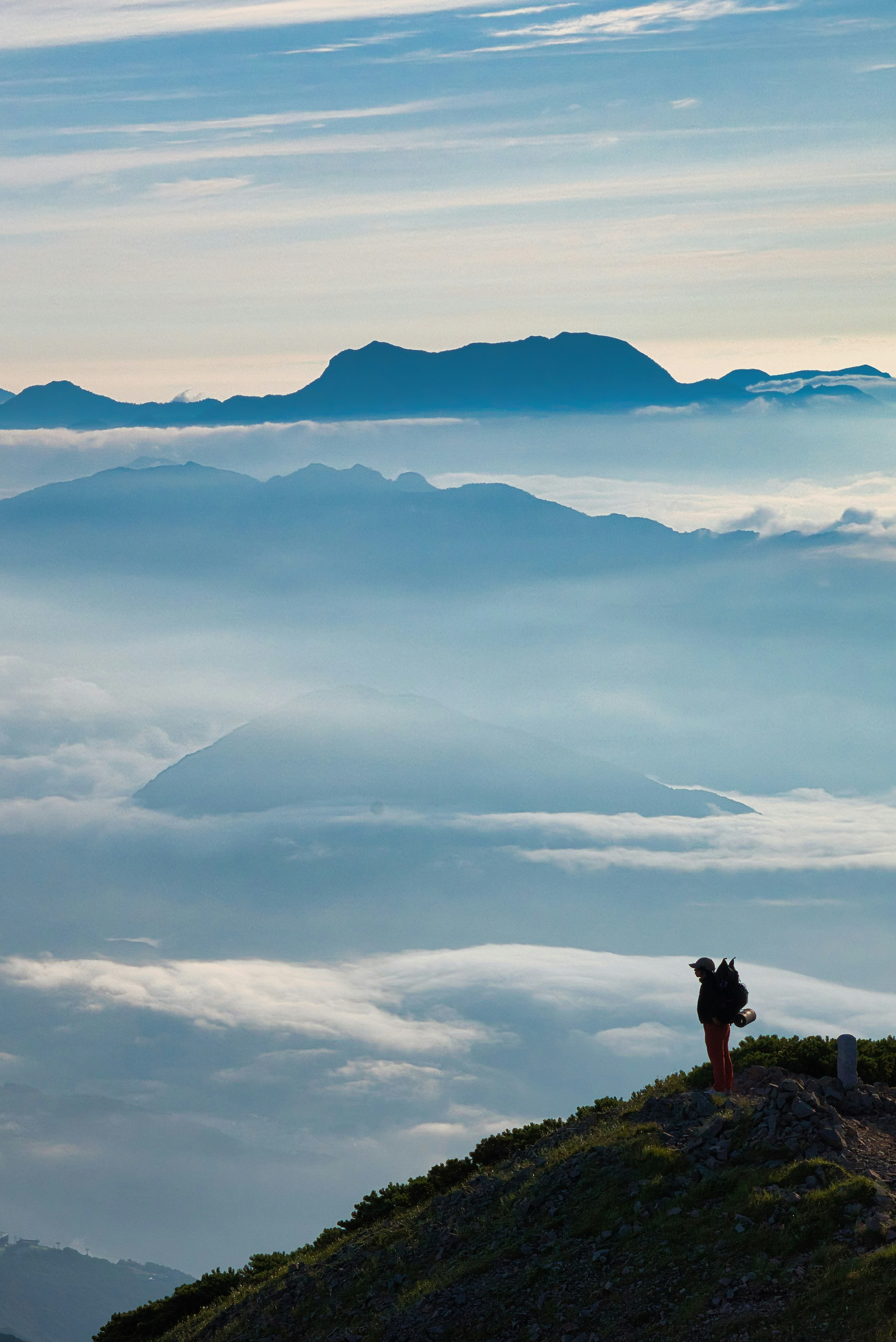 Seseorang berdiri di puncak gunung menghadap lautan awan