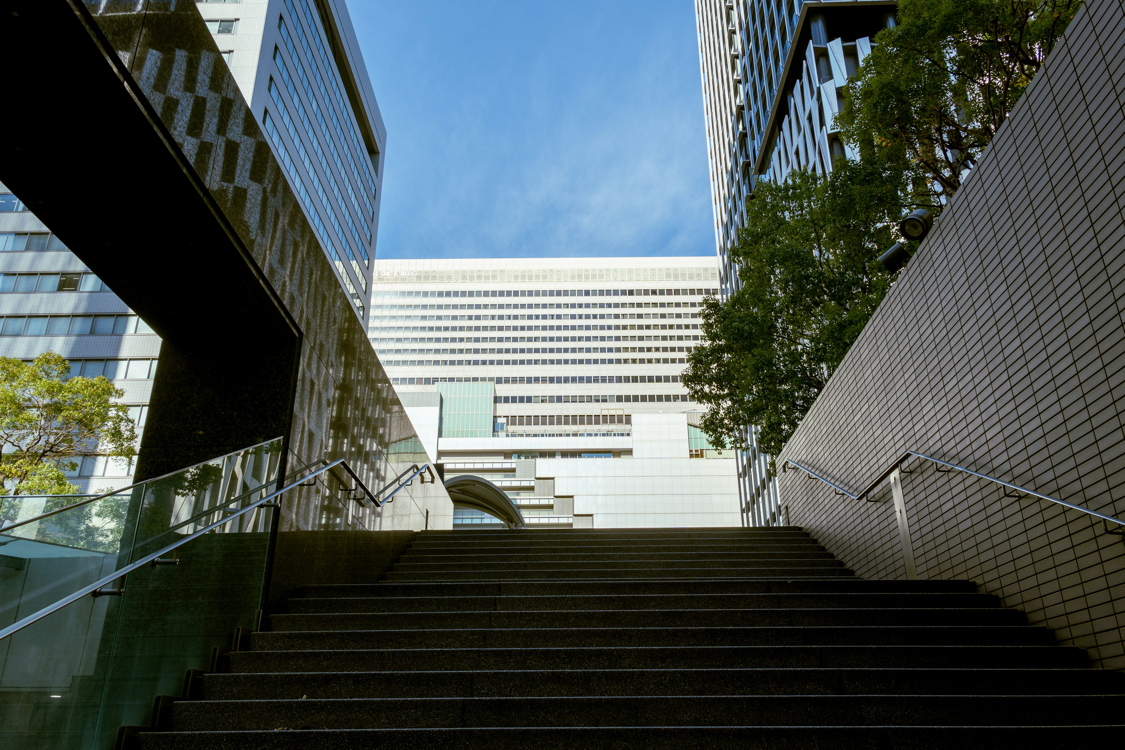 Pemandangan dari dasar tangga yang mengarah ke gedung modern dan langit biru