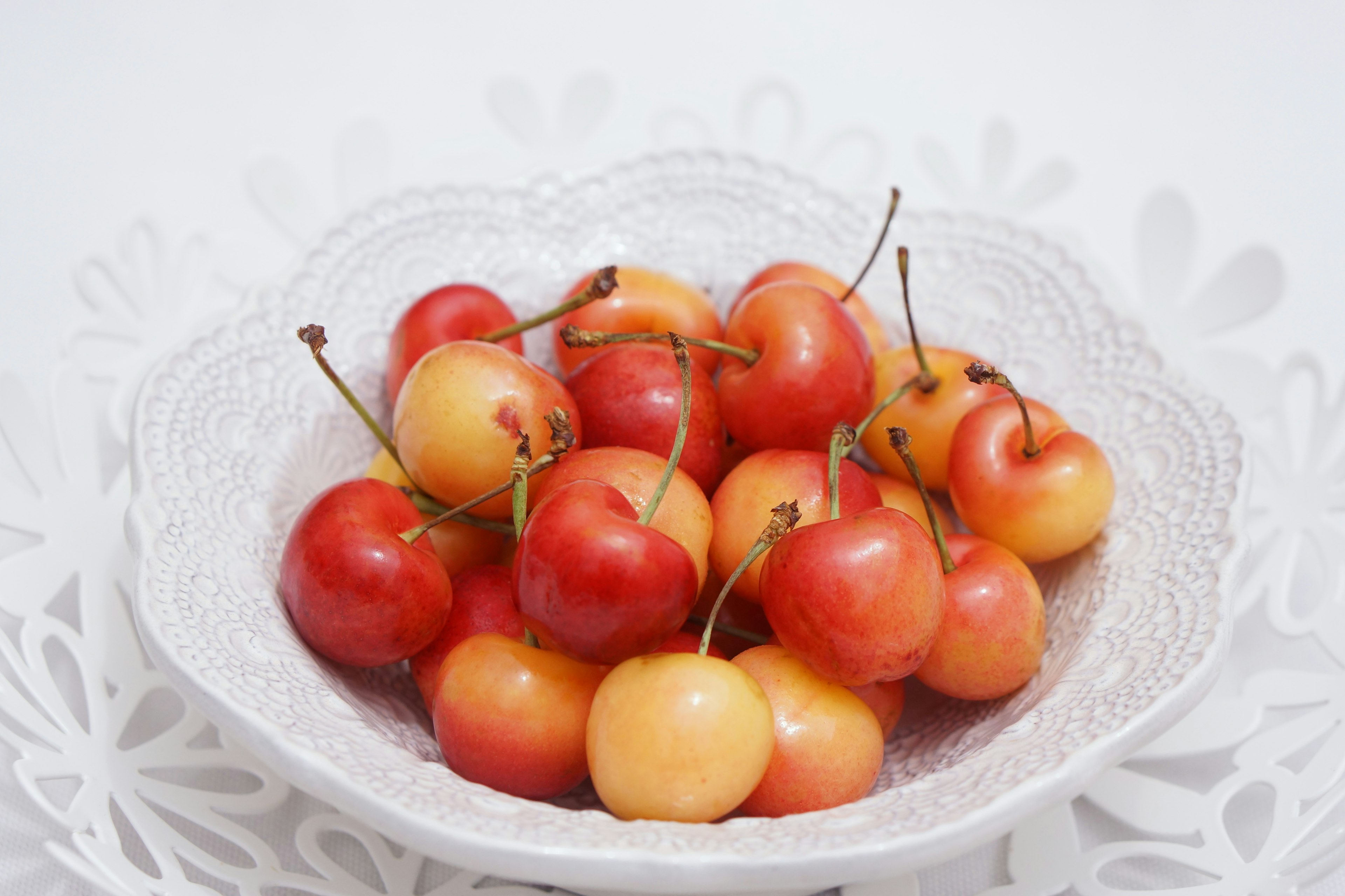 A bowl of red and yellow cherries on a white background