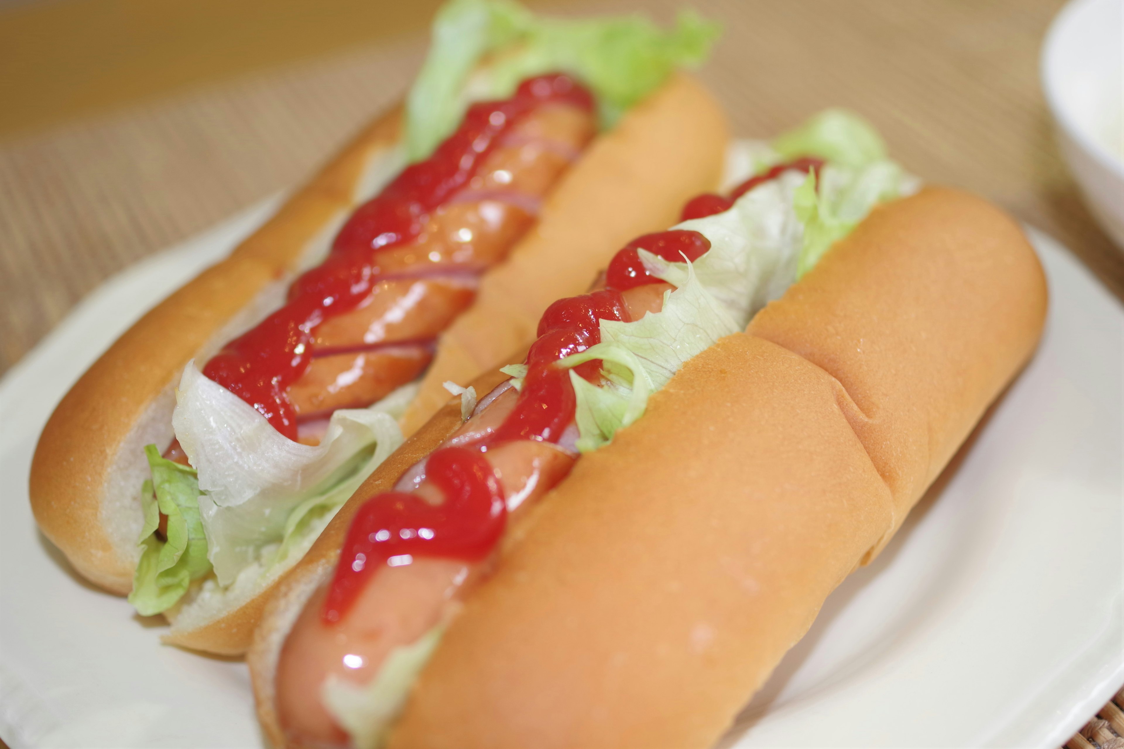 Dua hot dog dengan selada dan saus tomat disajikan di piring