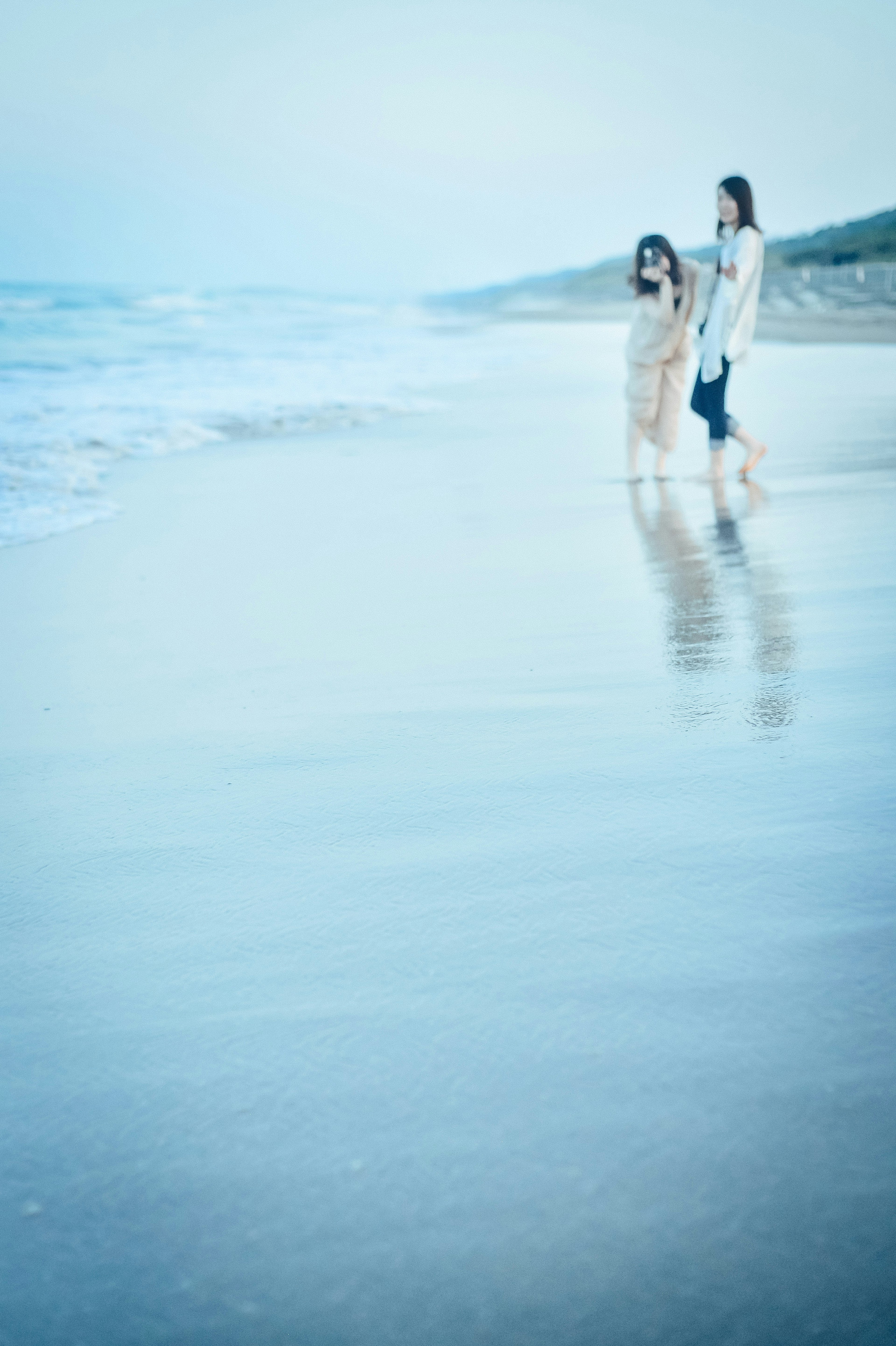 Silhouette of a parent and child walking along the beach with blue ocean and gentle waves