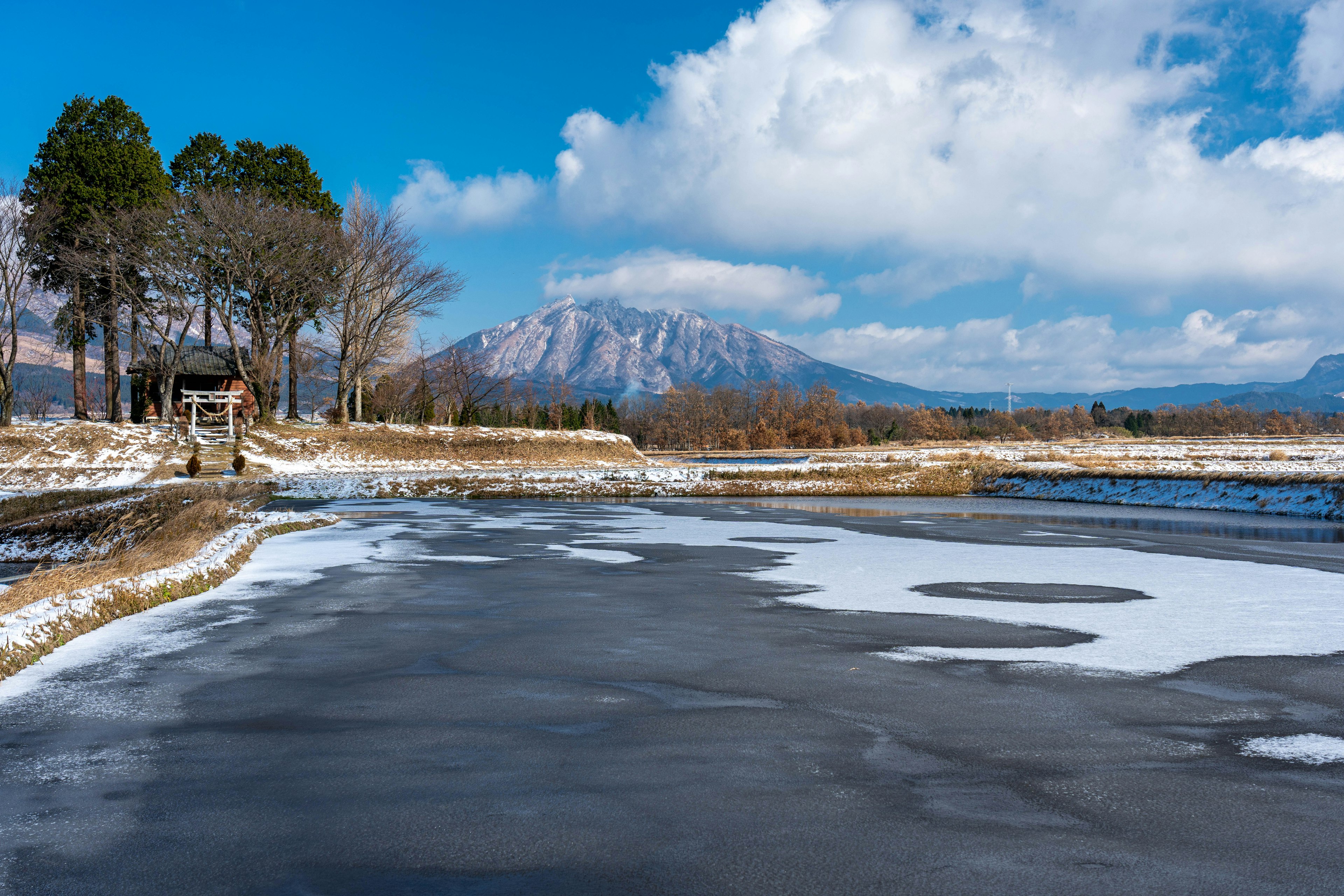 Paesaggio di lago innevato con montagne sotto un cielo blu e nuvole bianche