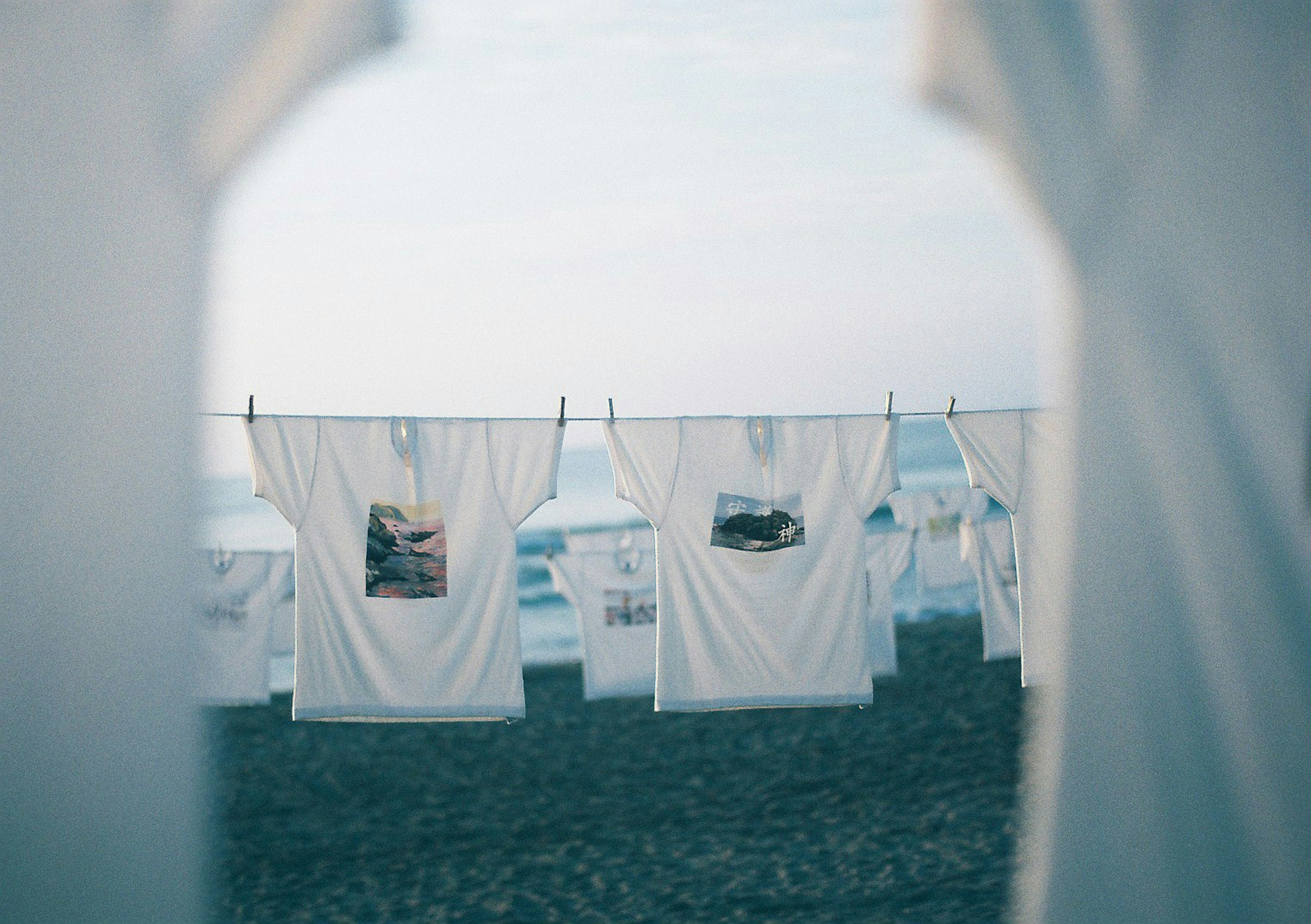 White t-shirts hanging on a clothesline by the beach with ocean and sky in the background