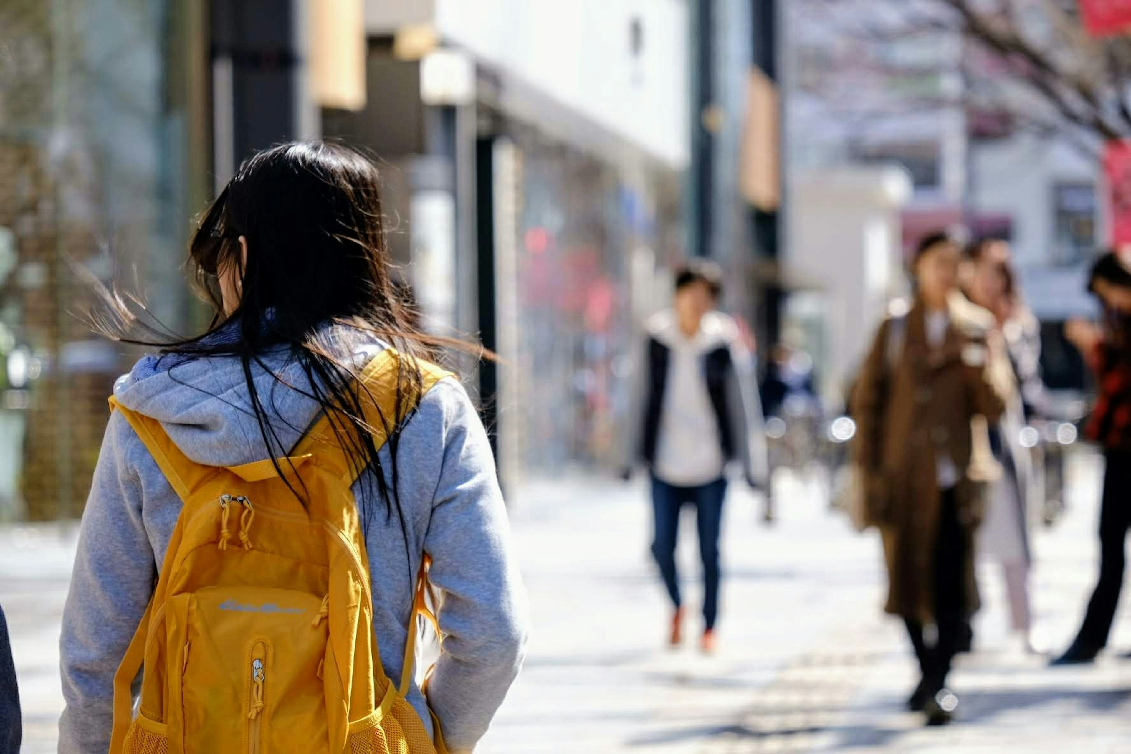 一个背着黄色背包的女人在繁忙的街道上走，周围有其他行人