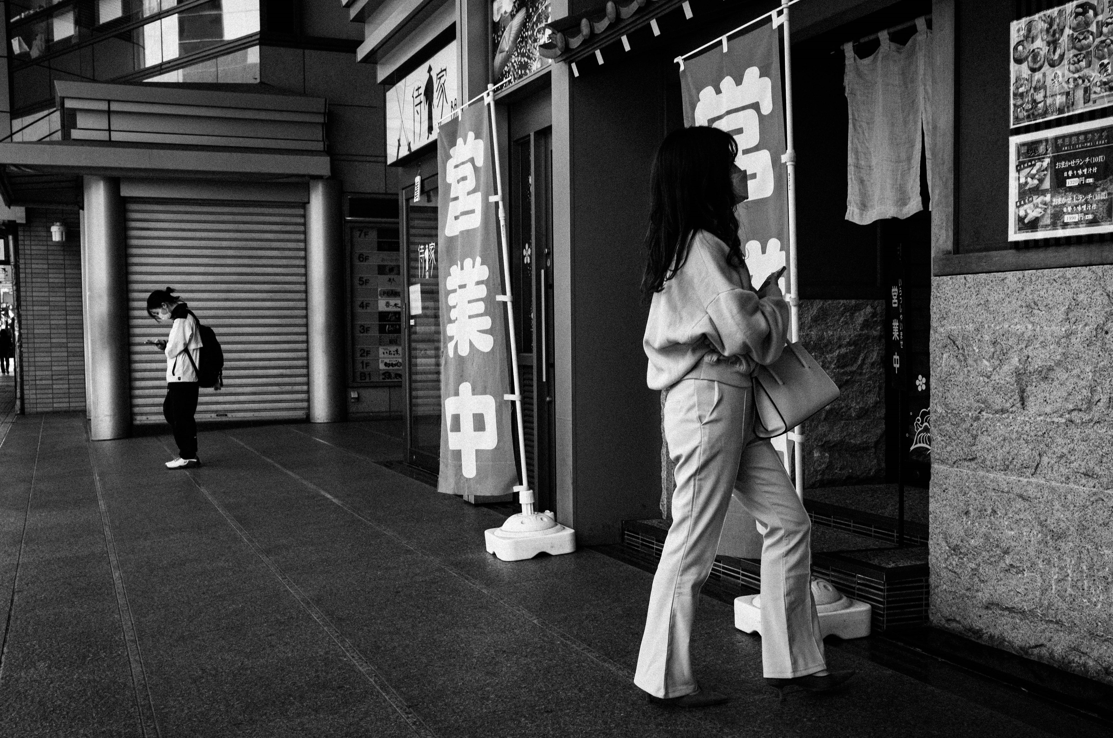 Black and white urban scene with a woman walking towards a store