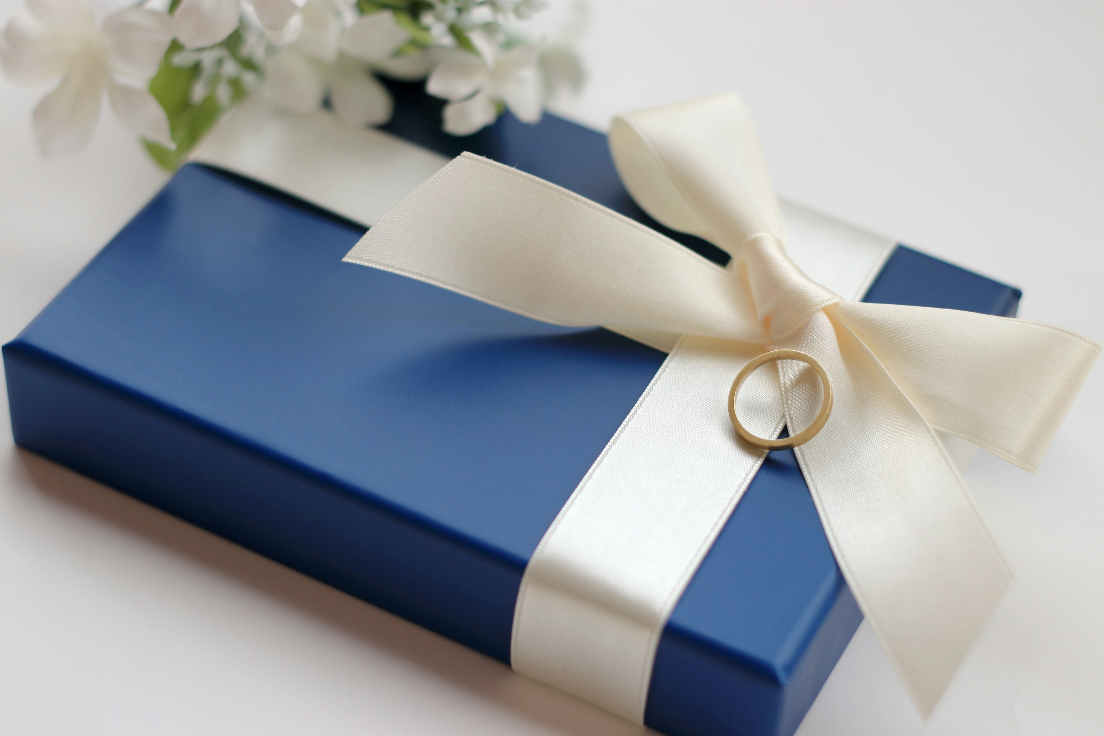 A blue gift box with a white ribbon and a ring attached