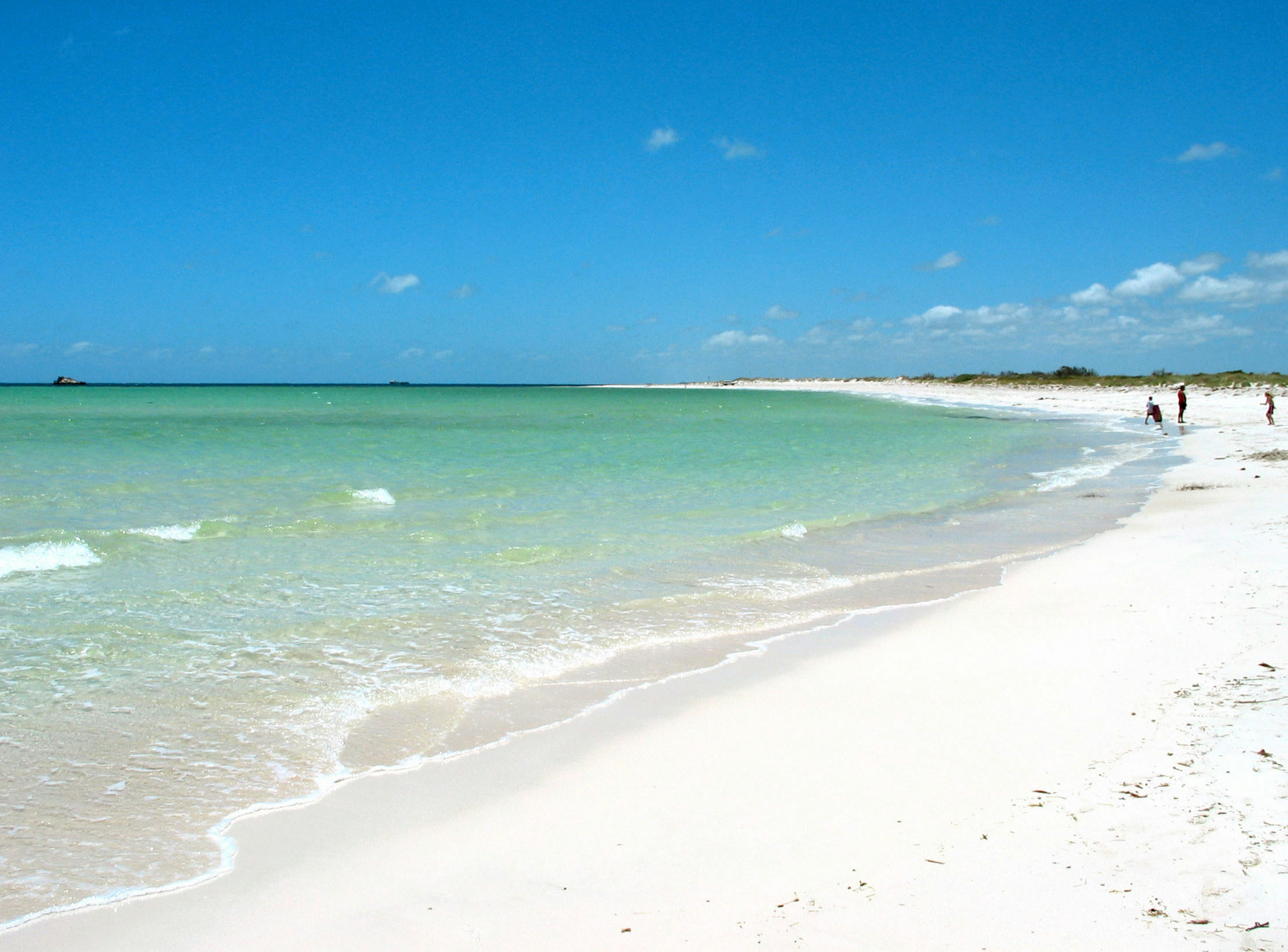 Vista panoramica di una spiaggia con acqua turchese e sabbia bianca sotto un cielo blu