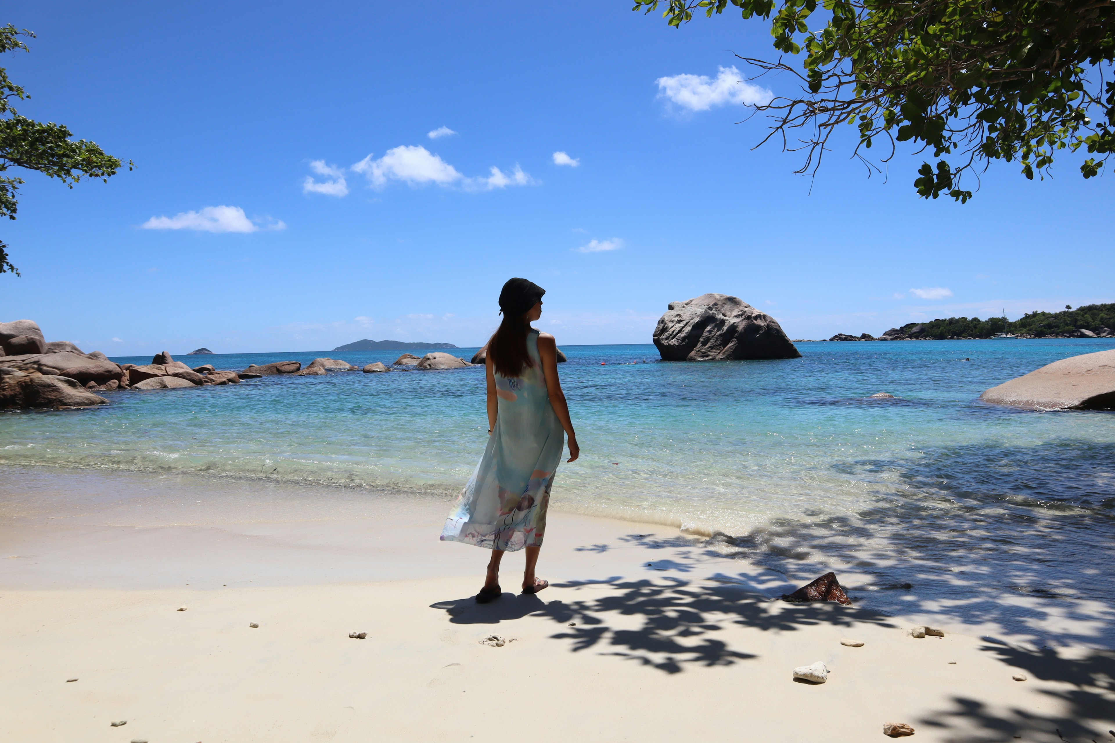 Siluet seorang wanita berdiri di pantai berpasir dengan laut biru