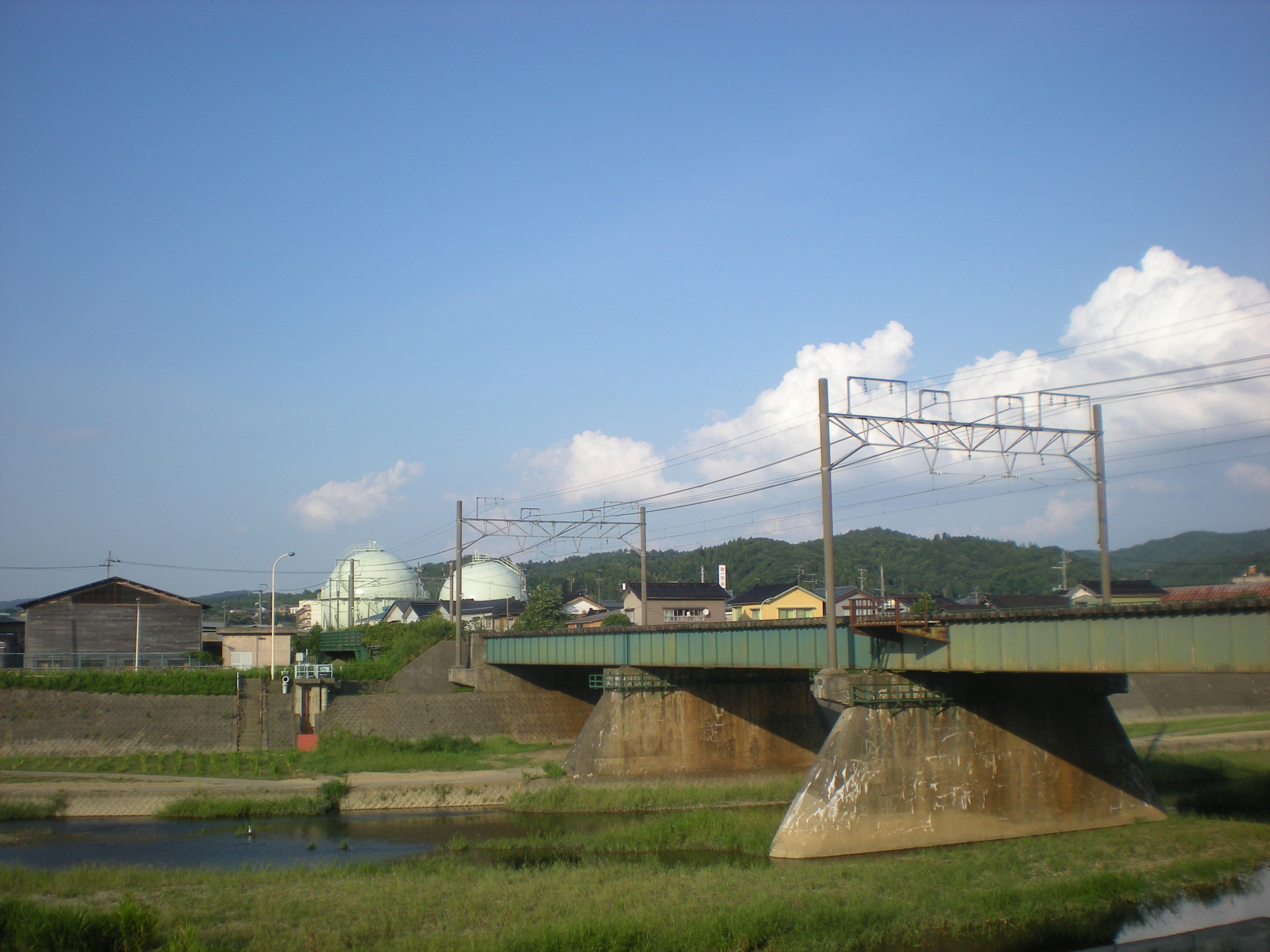 Brücke über einen Fluss mit grünen Hügeln und Industriegebäuden im Hintergrund