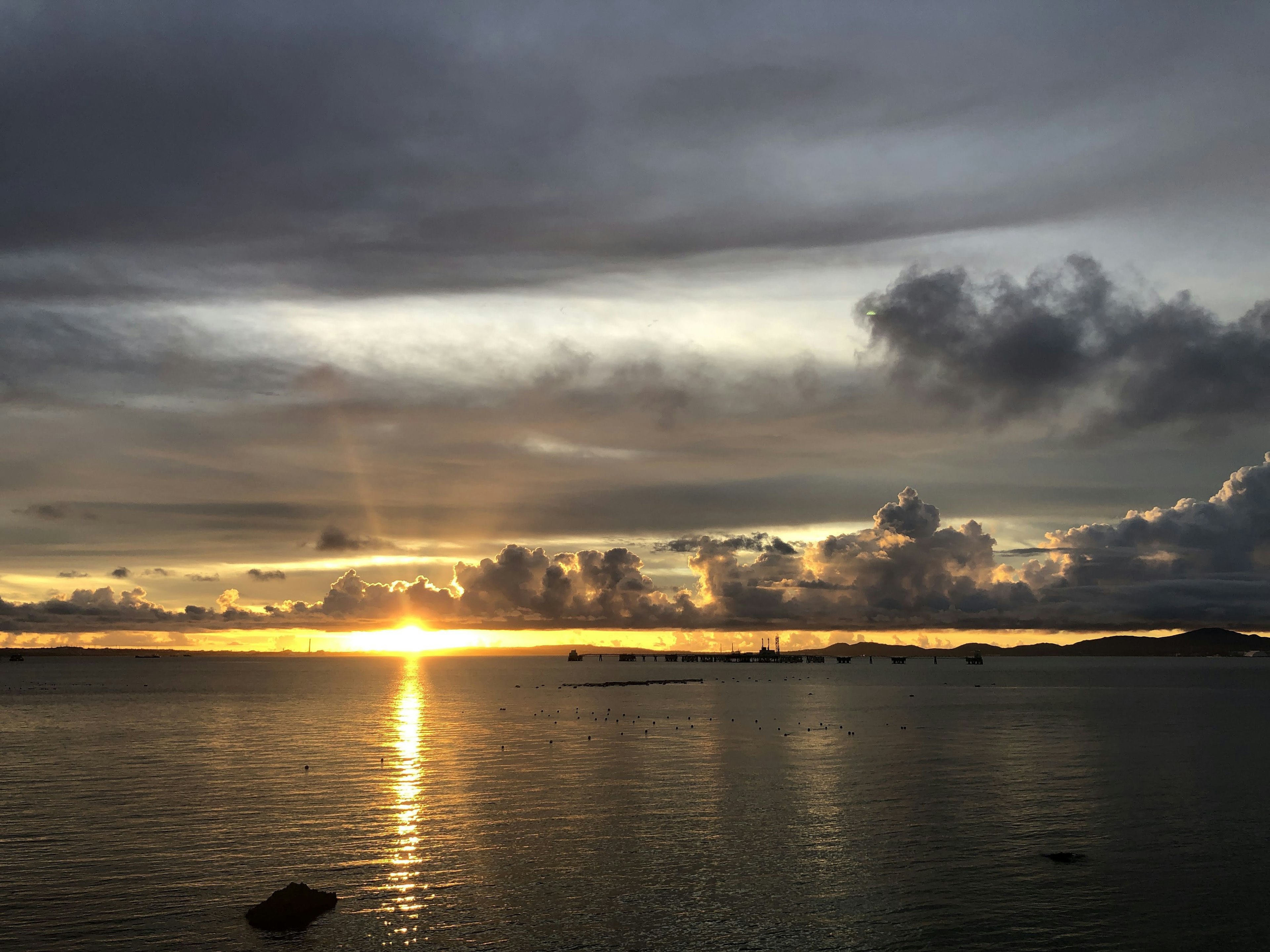 Sunset over the ocean with gray clouds and orange sunlight reflecting on the water