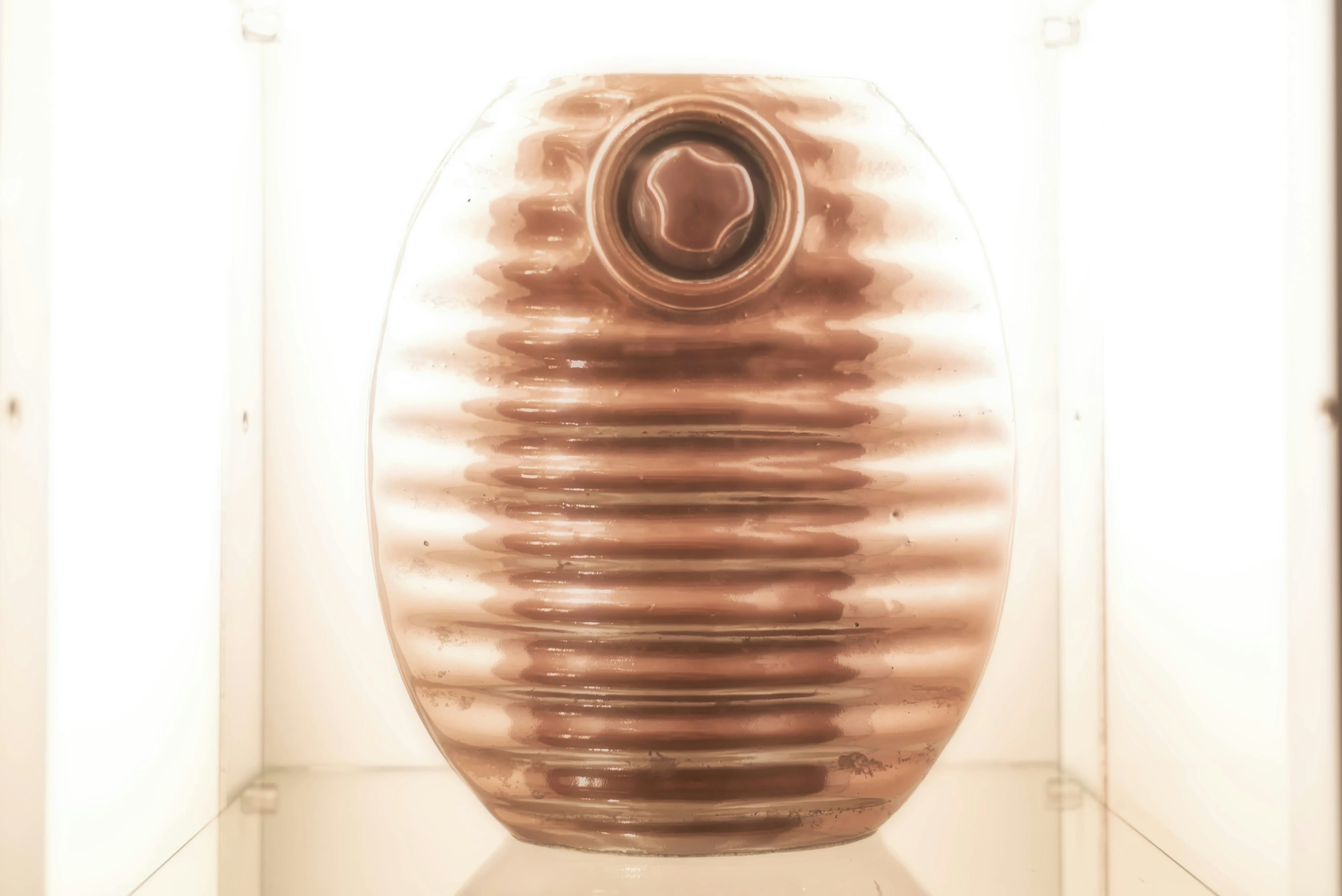 Vase en céramique rond et brillant avec texture nervurée exposé sur une étagère