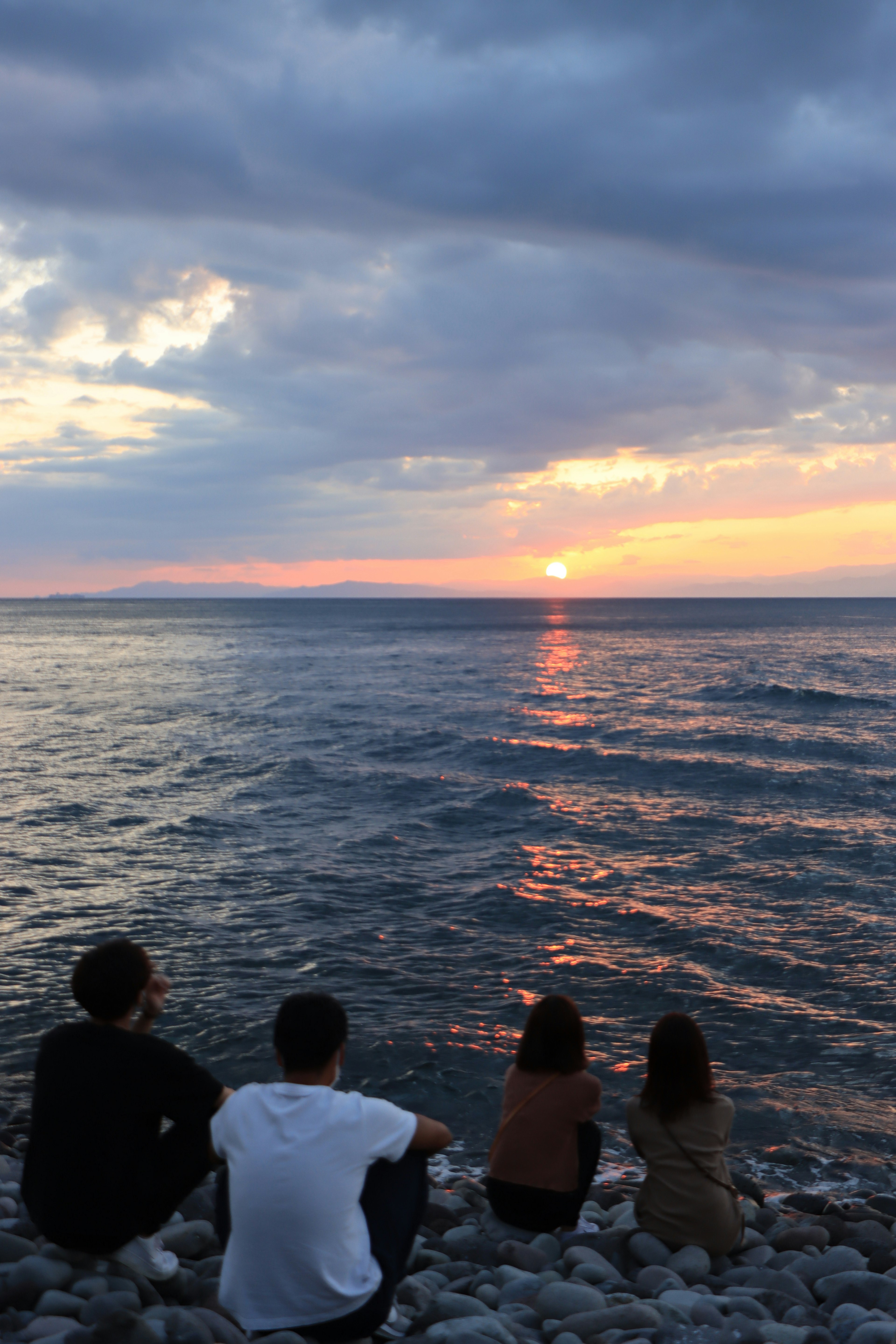 海辺で夕日を見つめる四人の友人たち